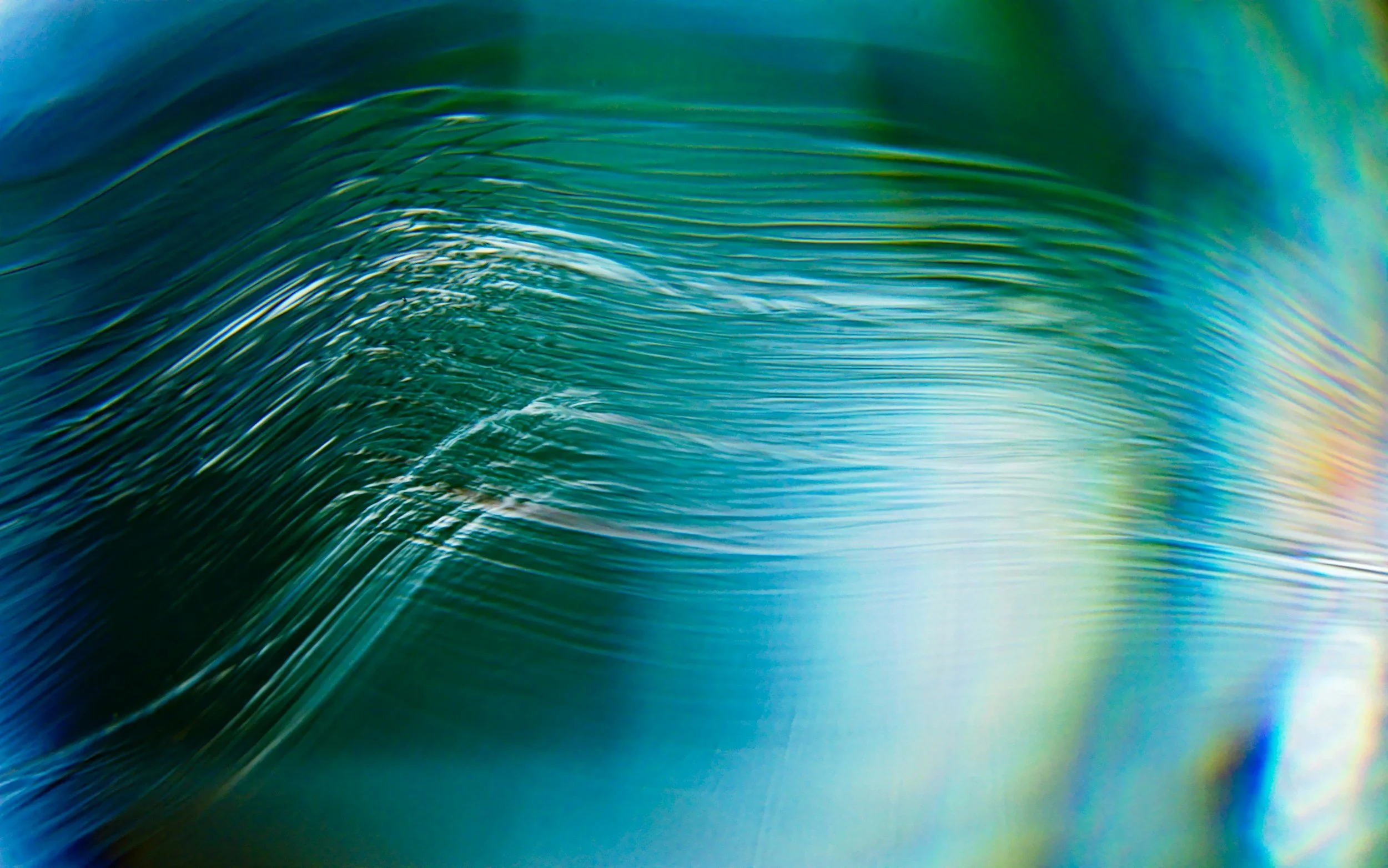 Close-up of a colorful, iridescent wave with smooth, flowing lines and rainbow-like hues.