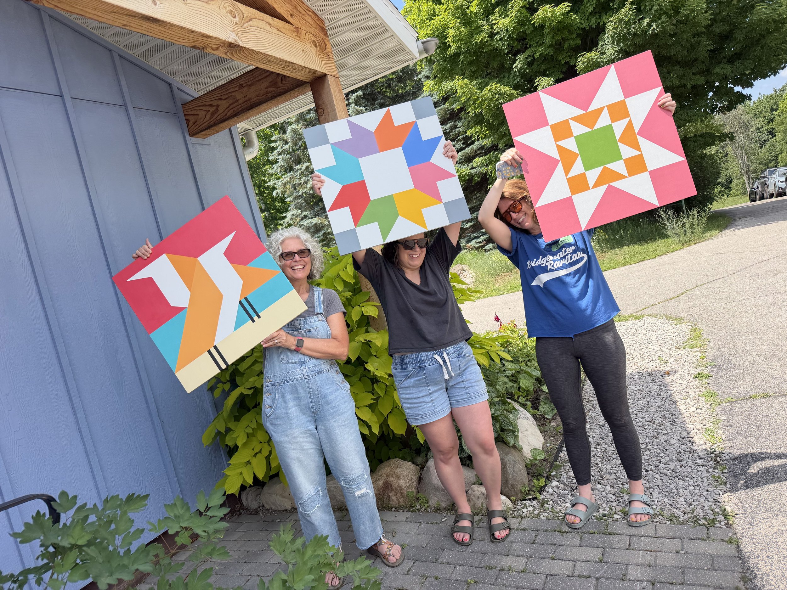 Three participants hold up their colorful barn quilts after a class taught by Maribeth.