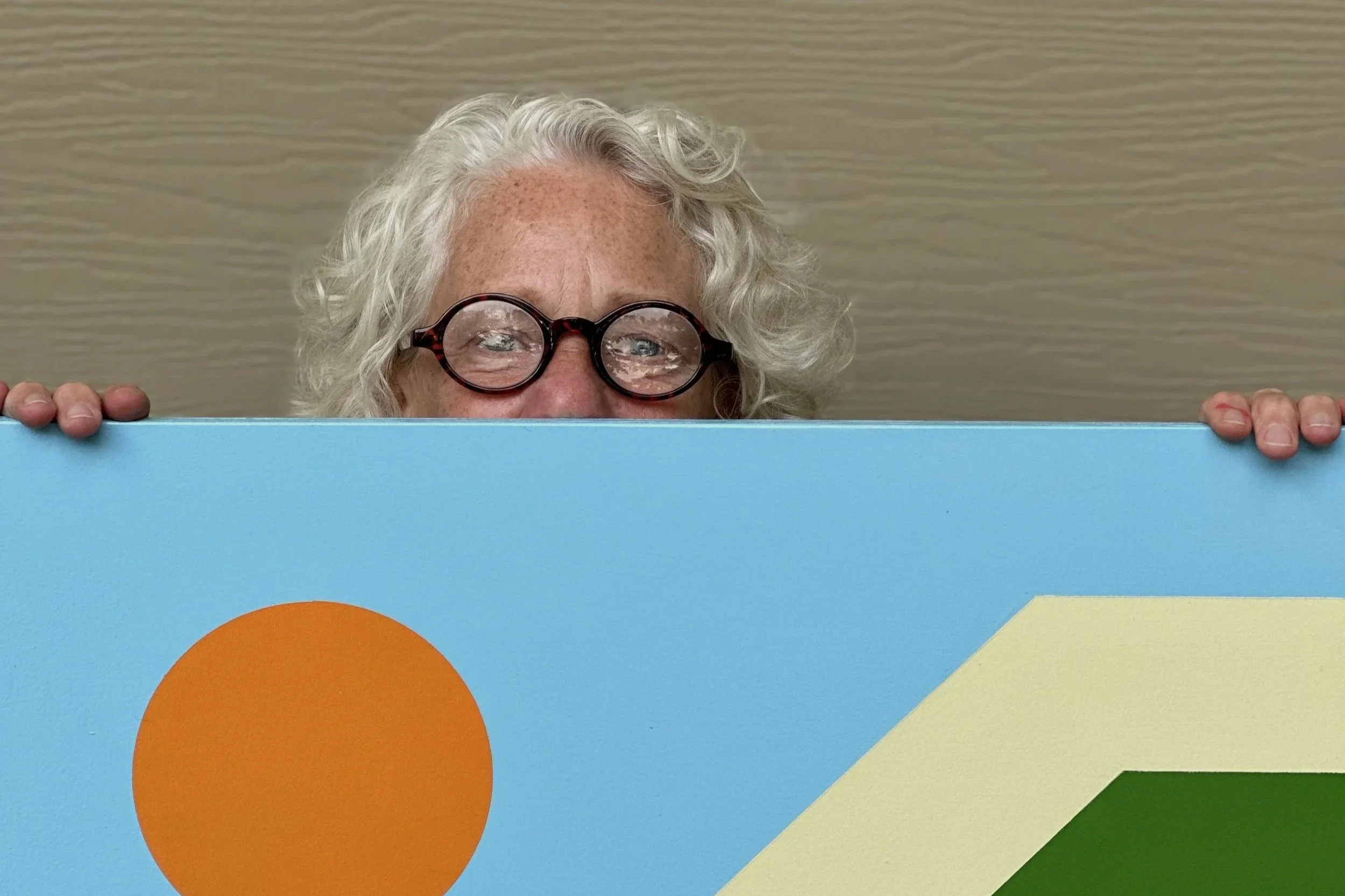 Photograph of a person peaking out from behind part of a barn quilt painting.