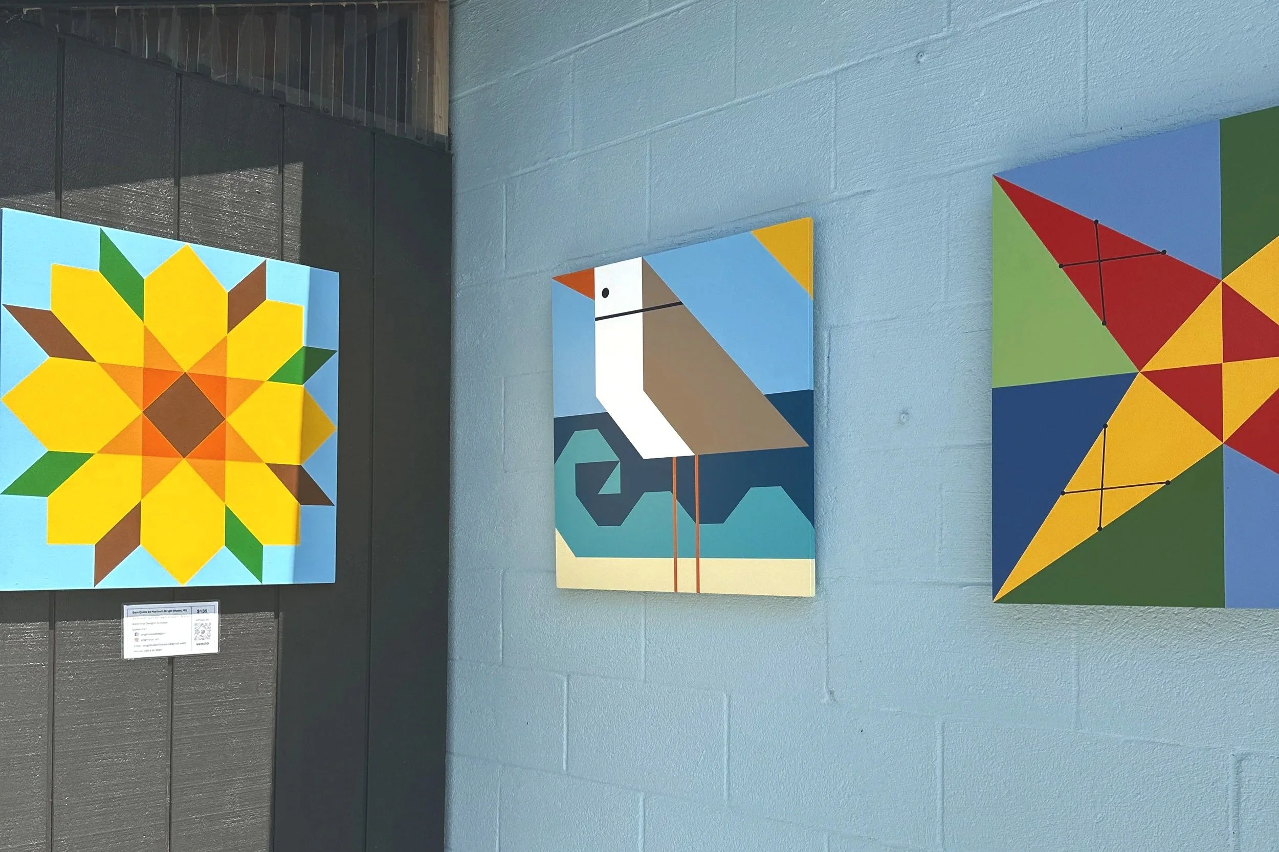 Photograph of three barn quilts displayed on the side of a building.