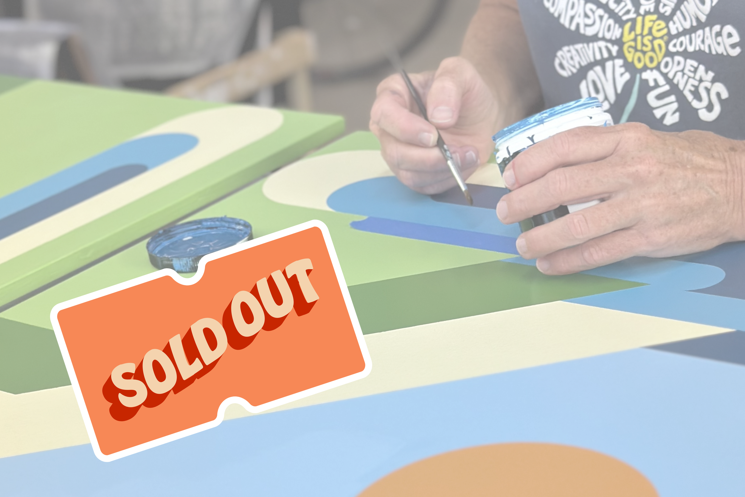 Photograph of hands painting a barn quilt with the words, "Sold Out" in front of the picture.