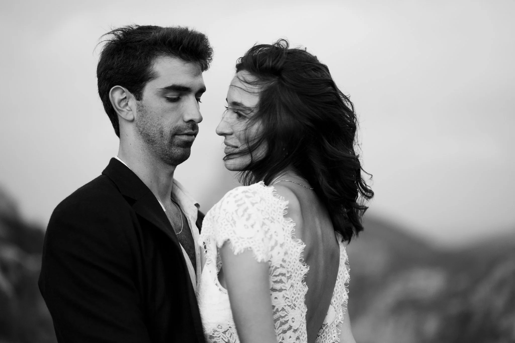 Ein Schwarz-Weiß-Foto eines Hochzeitpaares, das sich nahe steht, während ihrer Hochzeit, in einer lockeren und intimen Haltung, vor einem neutralen Hintergrund.