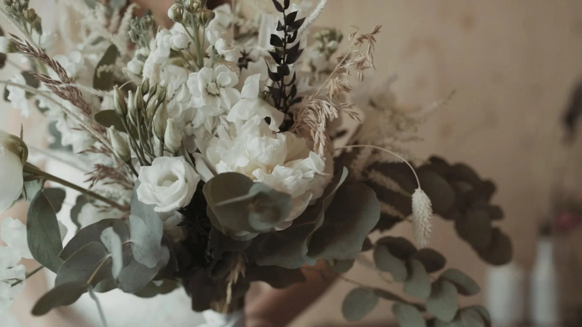 Brautstrauß aus weißen Blumen mit Blättern und Gräsern, dunkle und helle Blätter, unscharfer Hintergrund am Tag der Hochzeit.