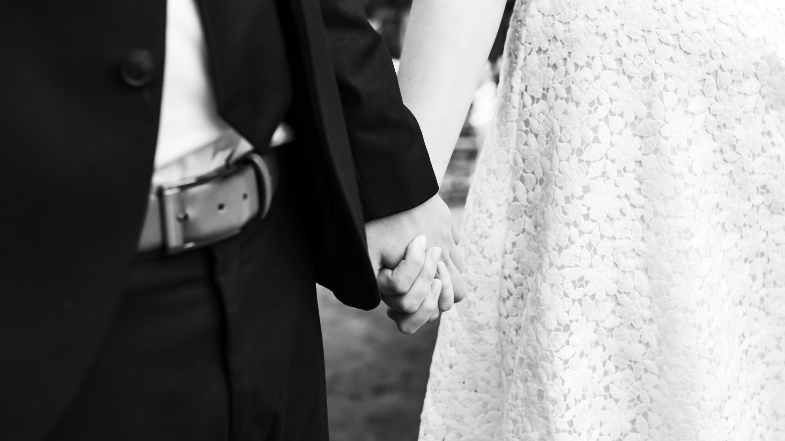 Nahaufnahme eines Hochzeitspaares, das sich an einer Hochzeit hält, die Hand des Mannes im schwarzen Anzug hält die Hand der Frau im weißen Kleid mit Spitze.
