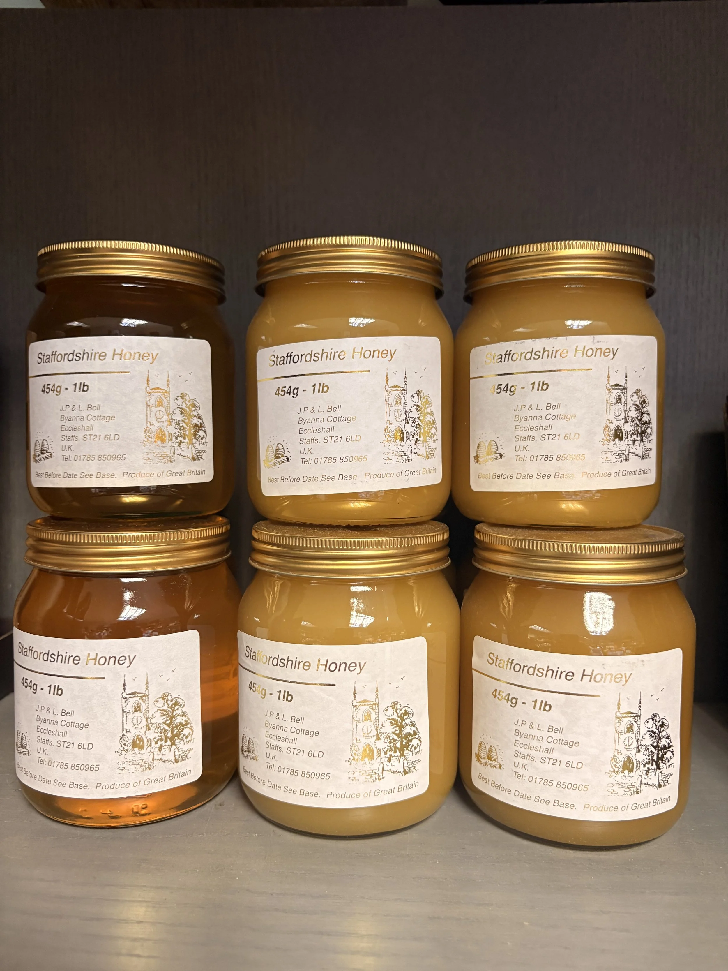 Three jars of Staffordshire Honey with white labels and gold lids, arranged on a shelf against a dark background.