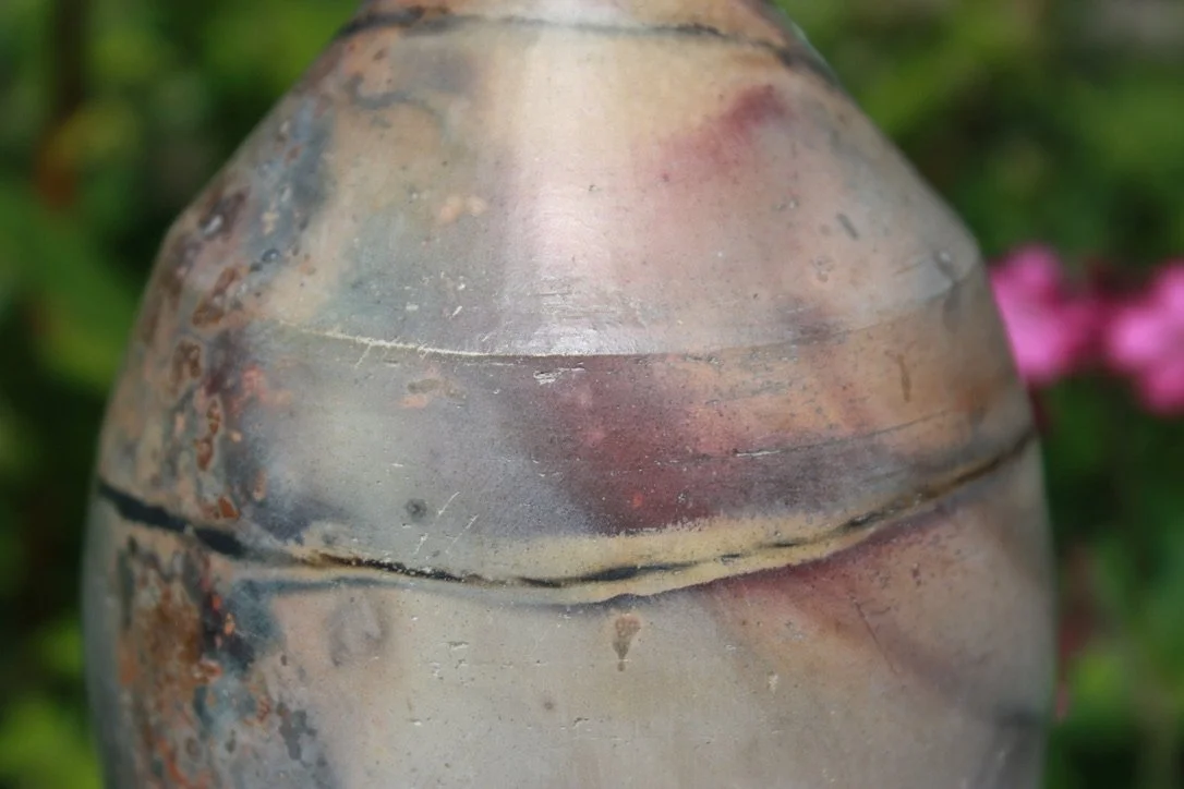 Close-up of a rusty, weathered metallic object with a round, tapered shape, against a blurred green and pink background.