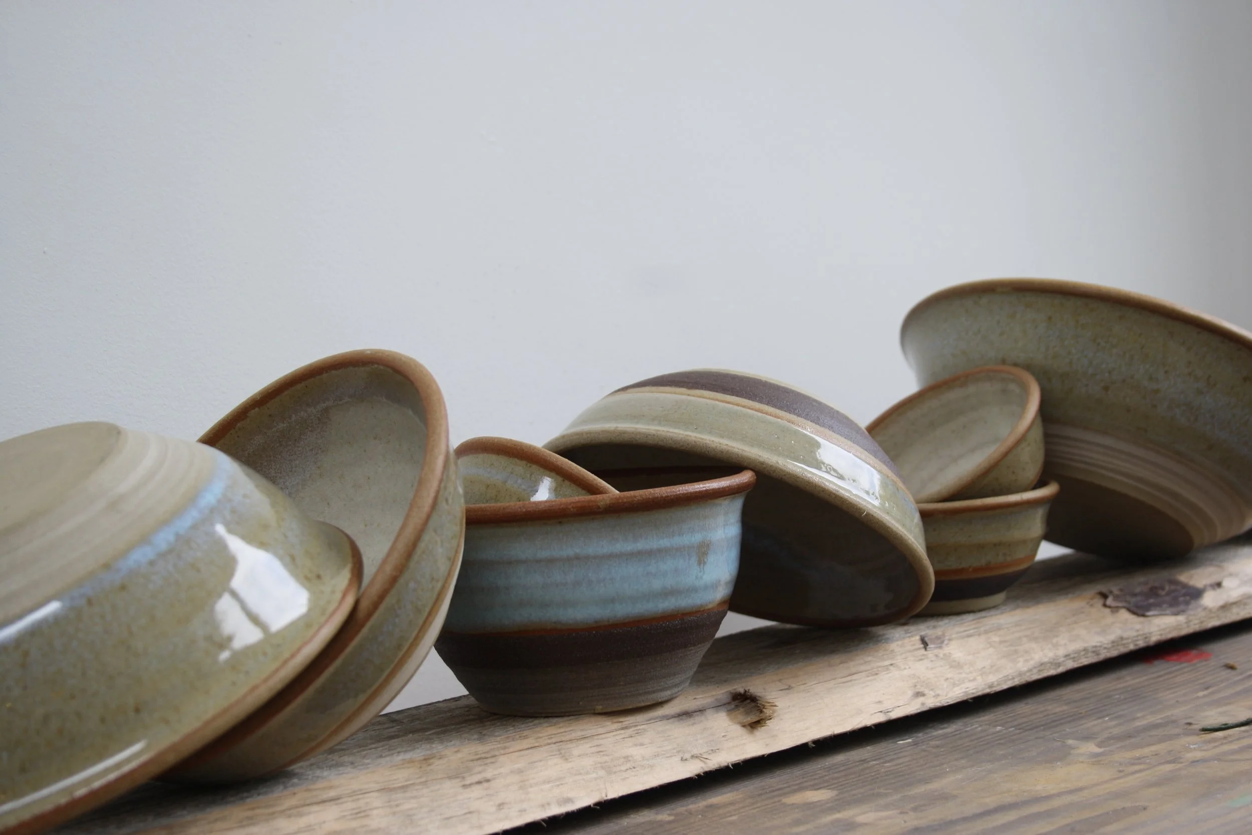 Stacked handmade ceramic bowls with earthy tones on a wooden surface against a plain white wall.