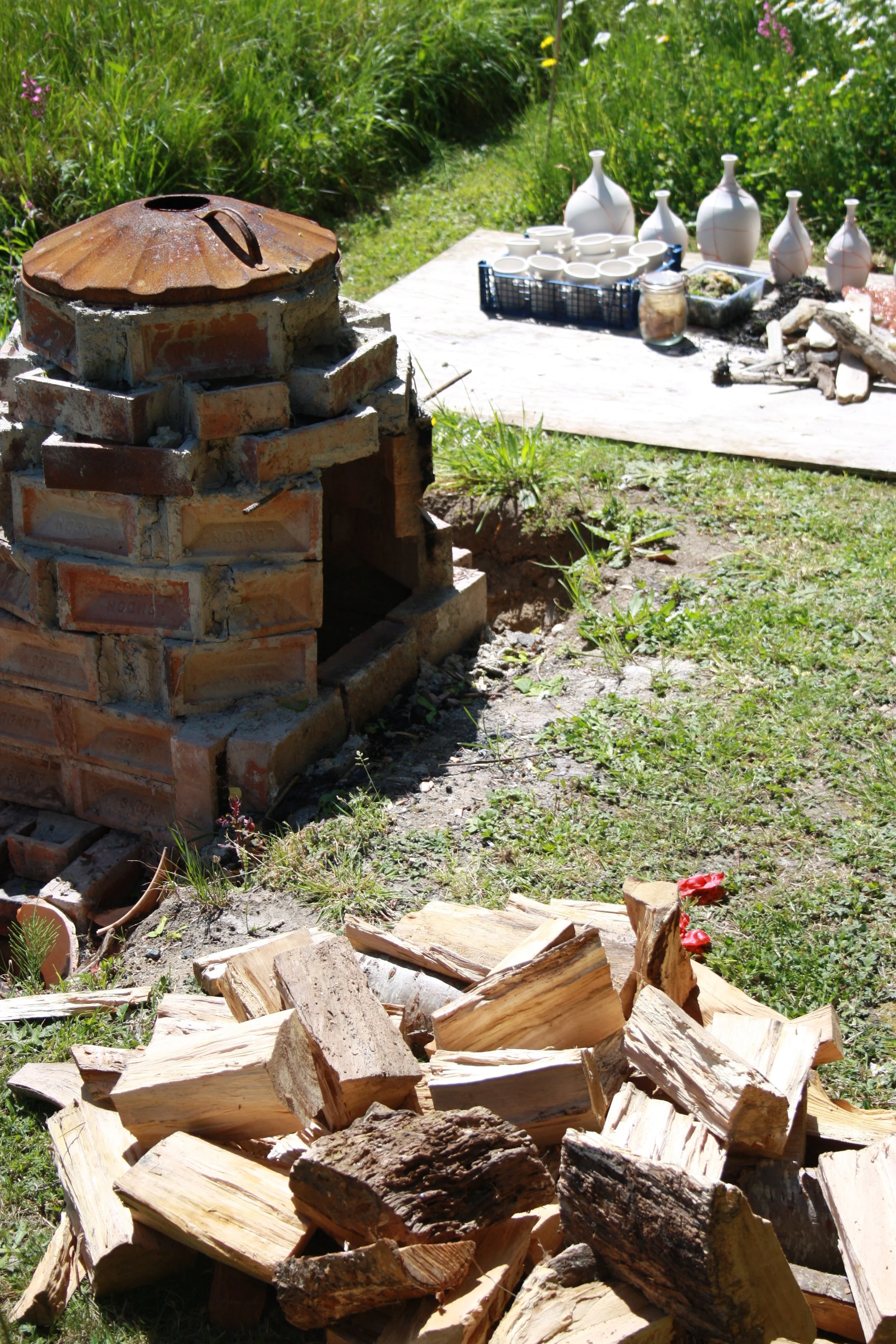 Wood is piled up high beside the hand built kiln. Created from red bricks, clay and straw this simple kiln traps in the sea of the fire, and allows me to control the airflow through the kiln. This allows for a long, hot, slow firing for maximum effec