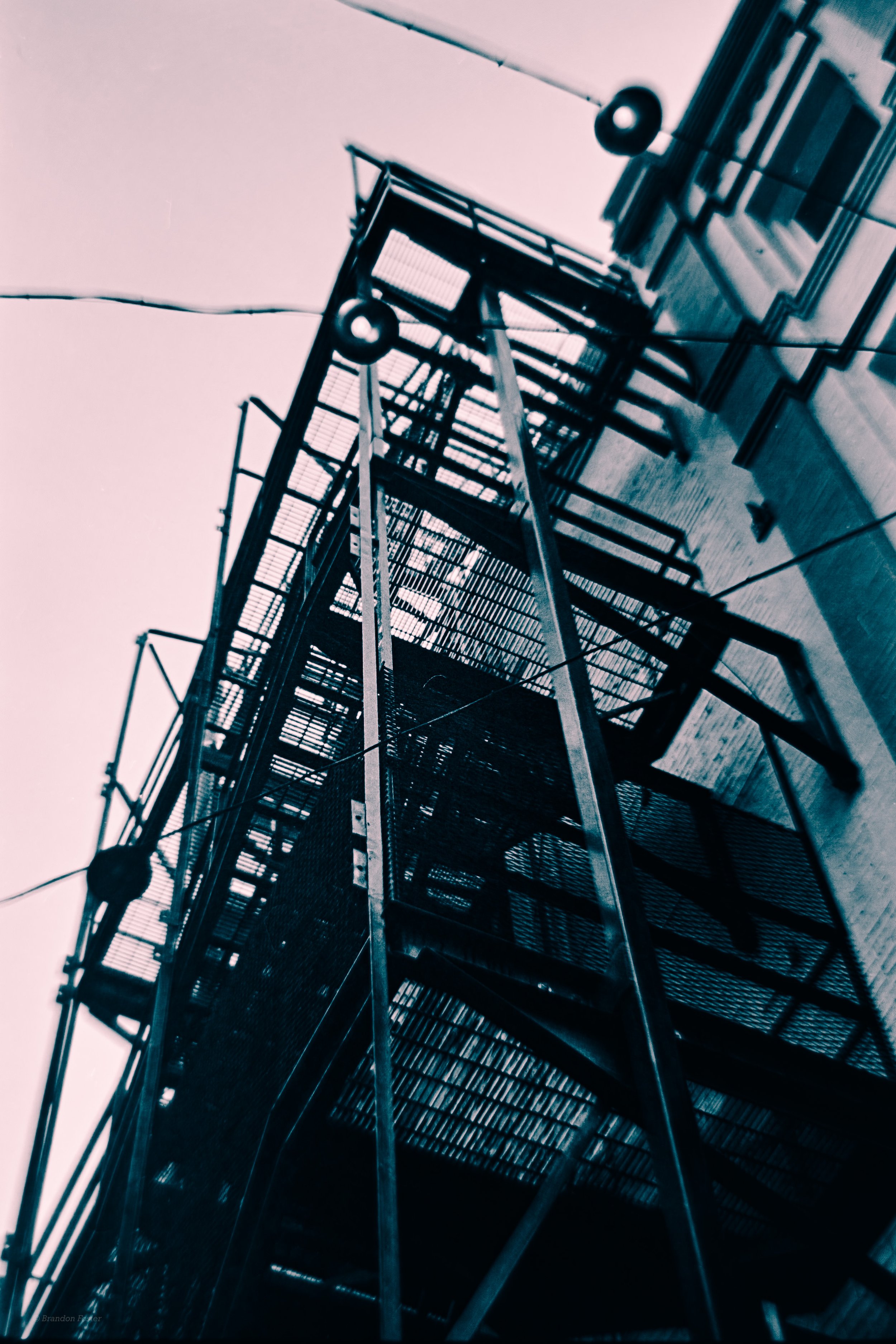 Looking up at a tall fire escape with metal stairs and railings attached to the side of a building on a clear day.