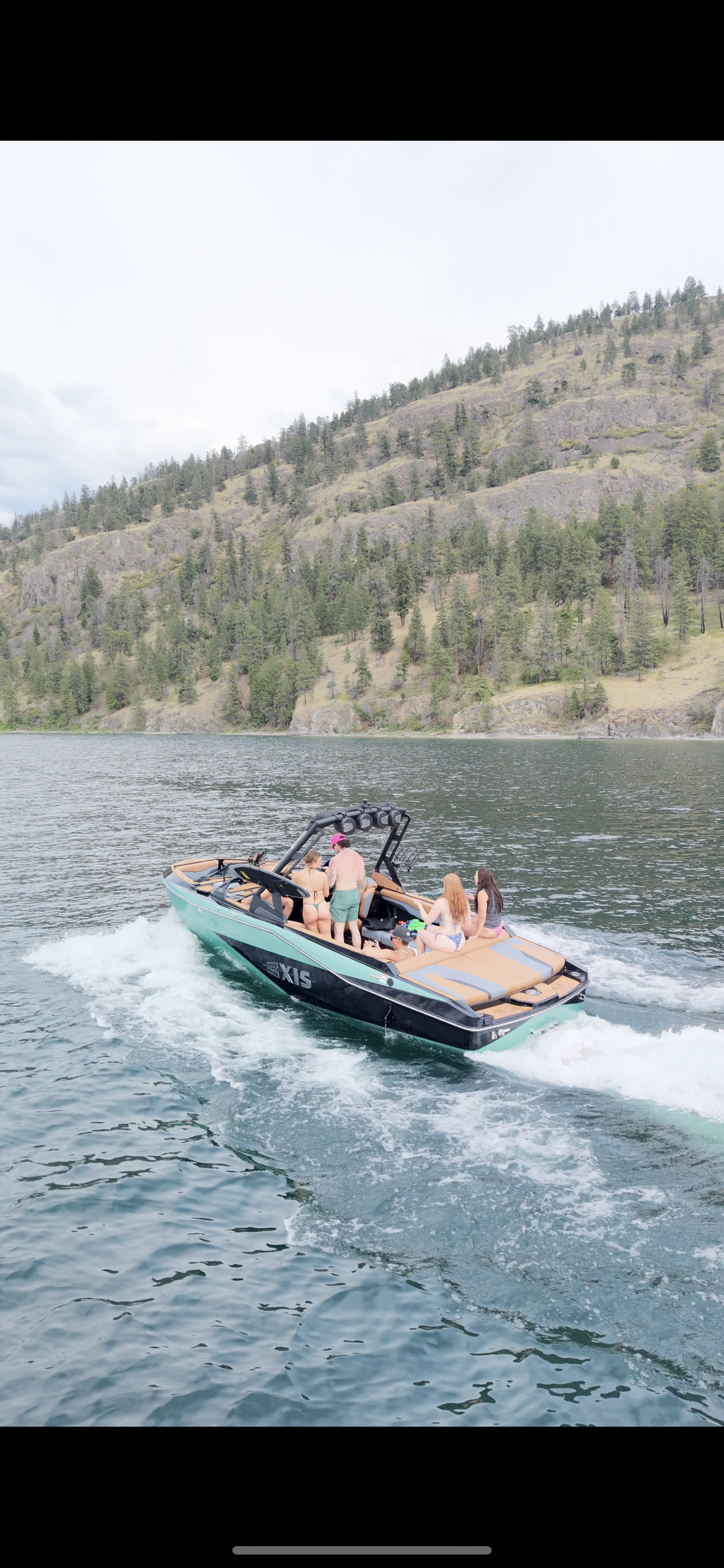 People enjoying a boat ride on a lake with a backdrop of forested hills and mountains.