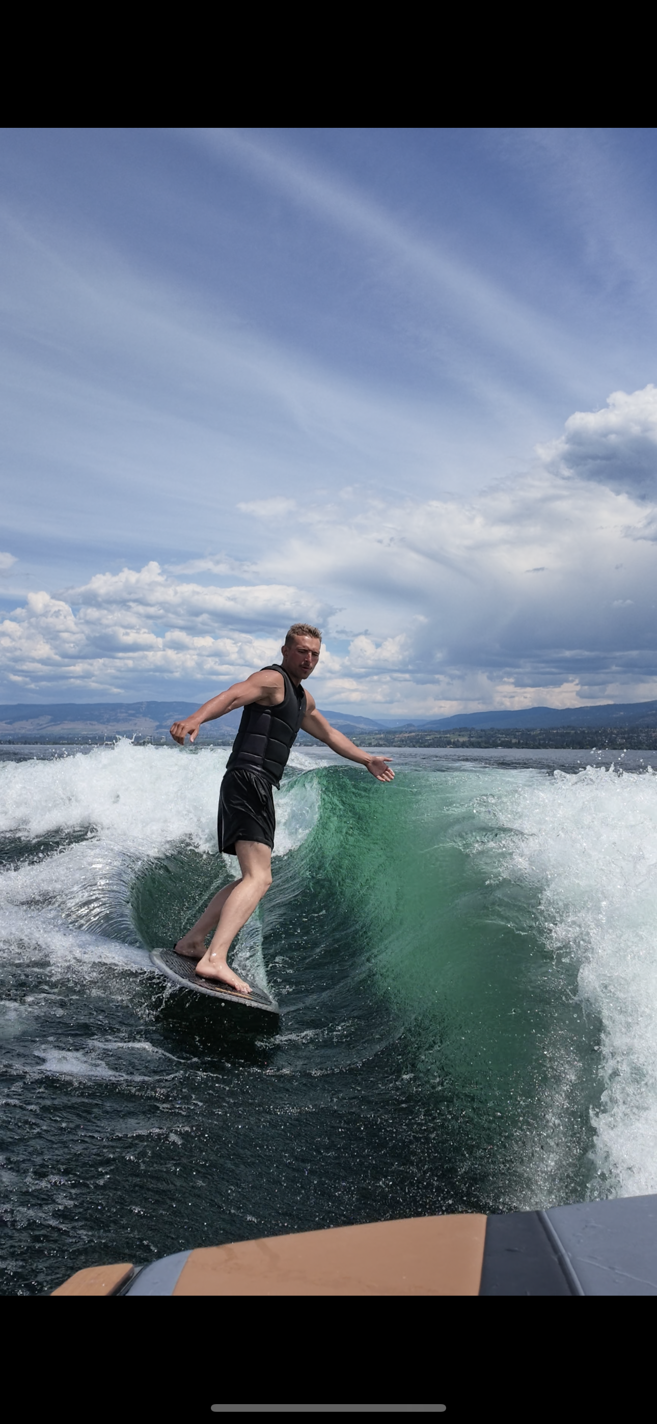 A man surfing on a green wave on a body of water under a partly cloudy sky.