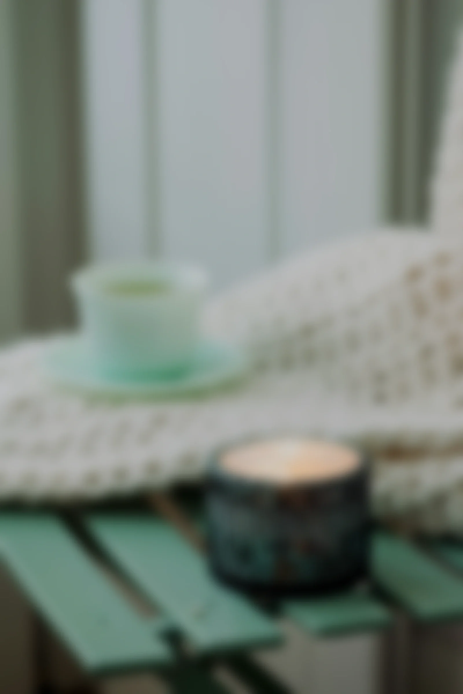 A blurred image of a blanket with a cup and a black electronic device on a surface.