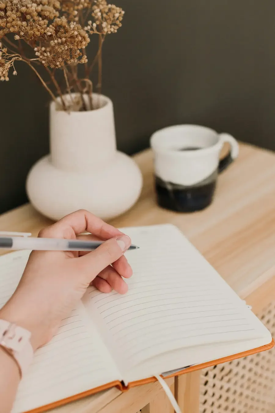 Person writing in a journal beside a cup of coffee