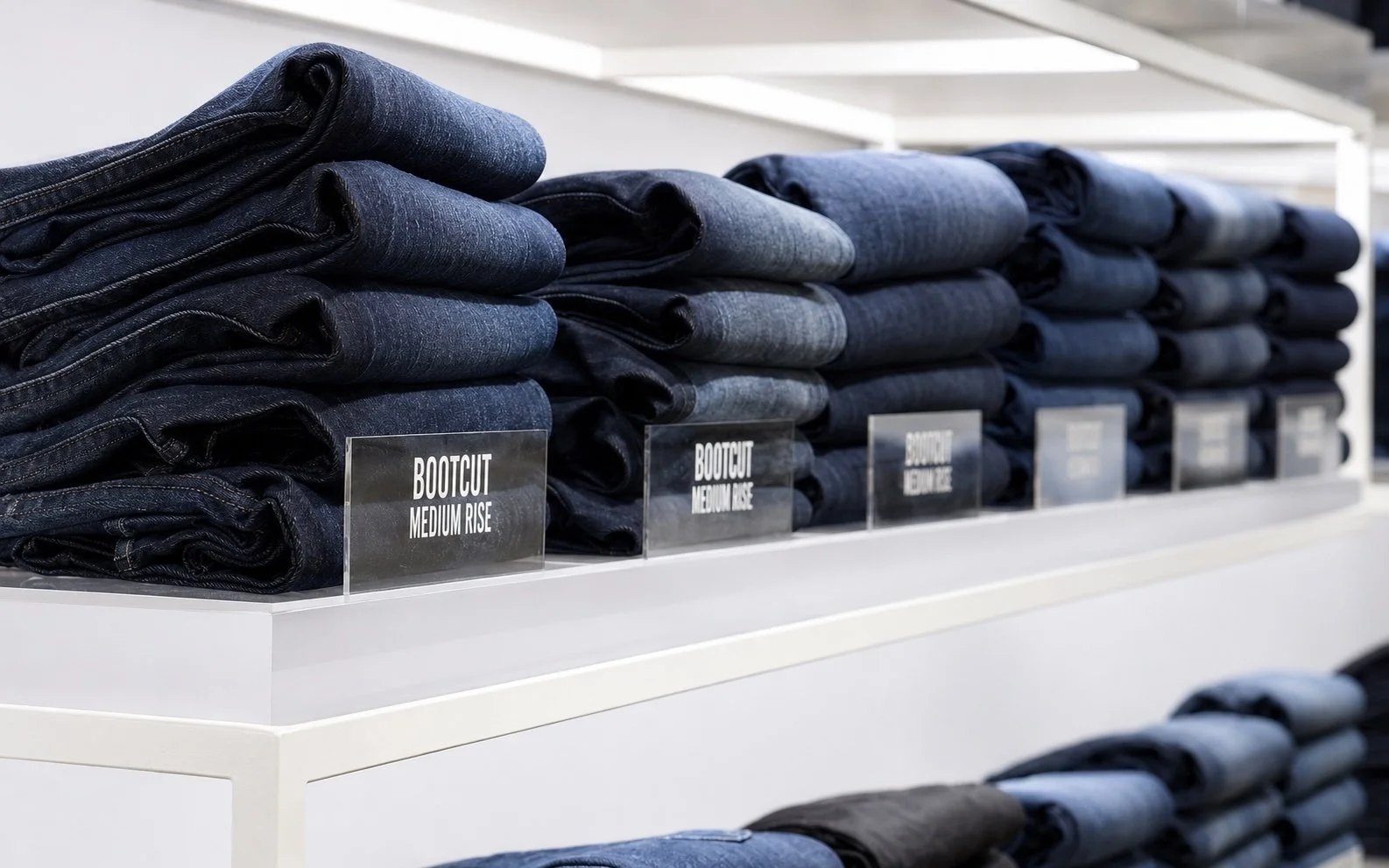 Stacks of folded jeans on a white store display with labels indicating different styles such as medium rise.