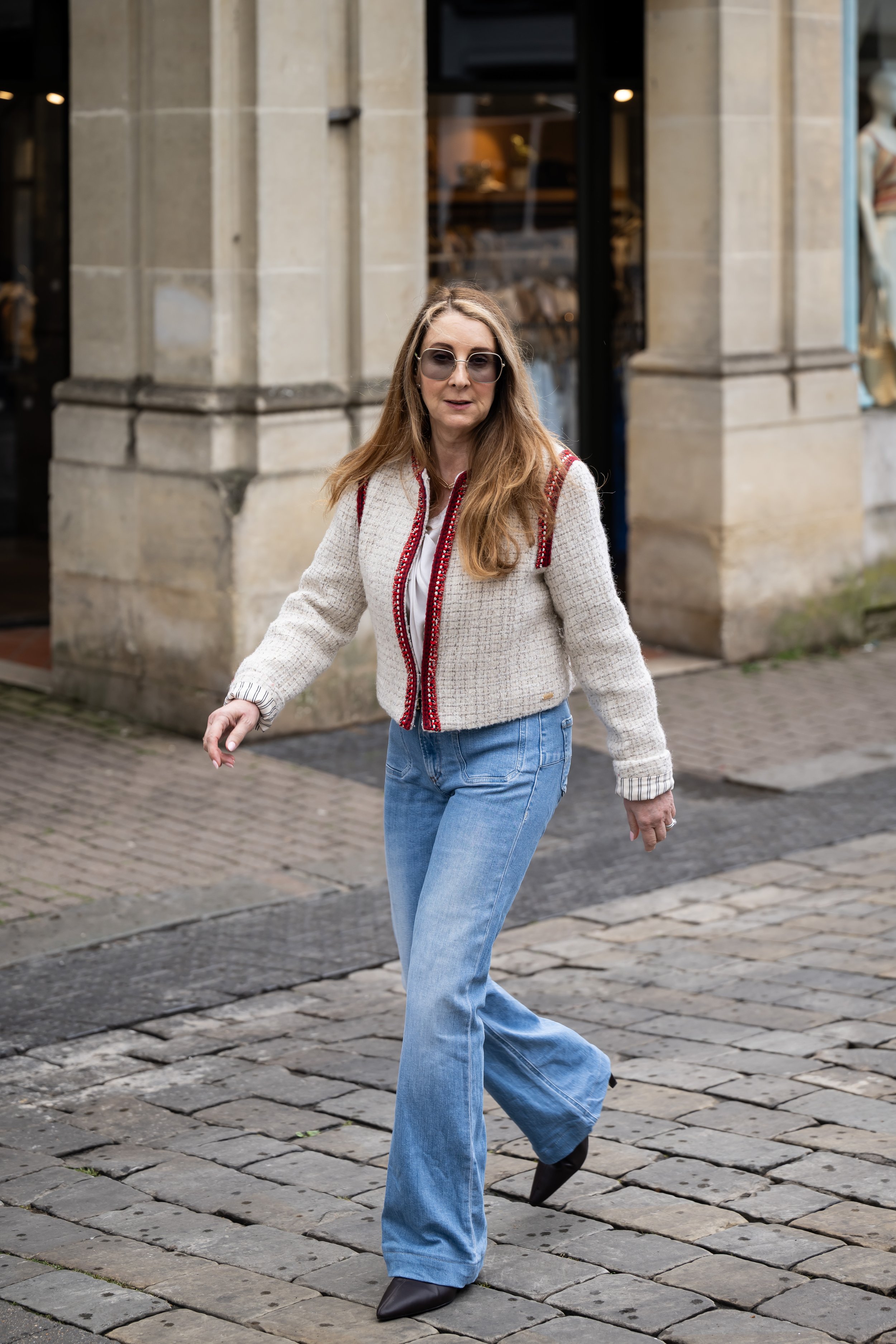 Sam Remer, denim-first personal stylist, walking through a shopping street in flare jeans and a cream jacket