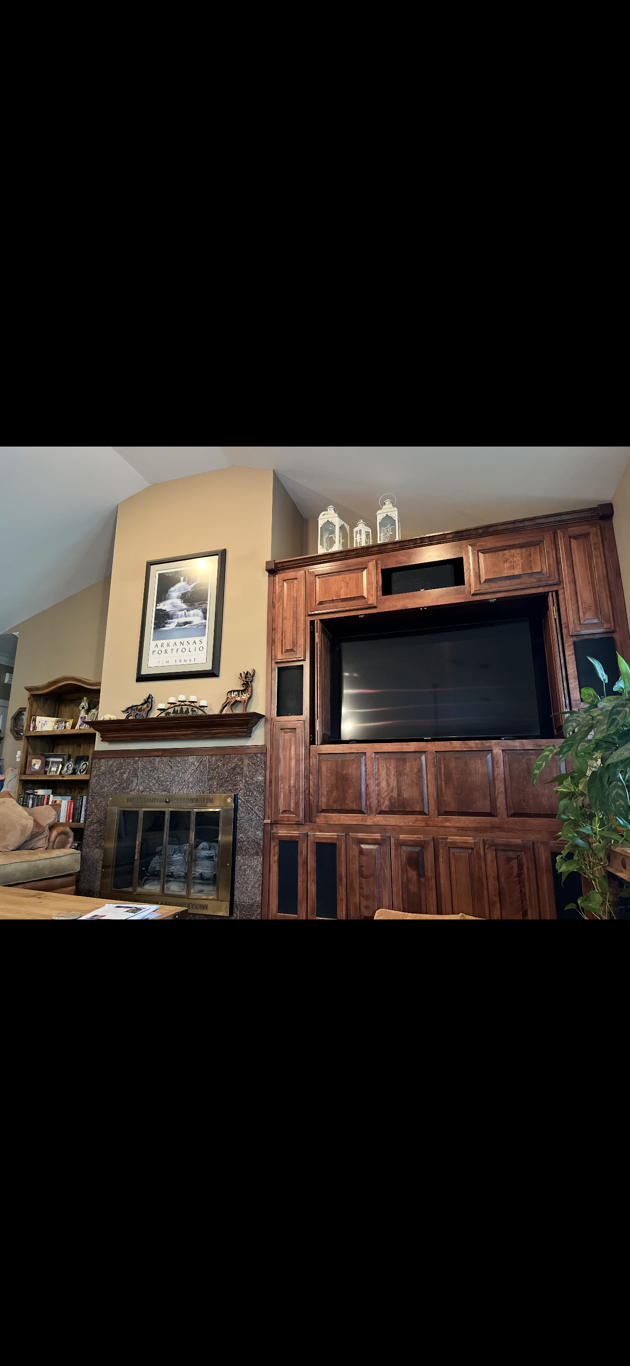 Living room with a fireplace, wooden entertainment center, and a TV, decorated with framed artwork, lanterns, and plants.