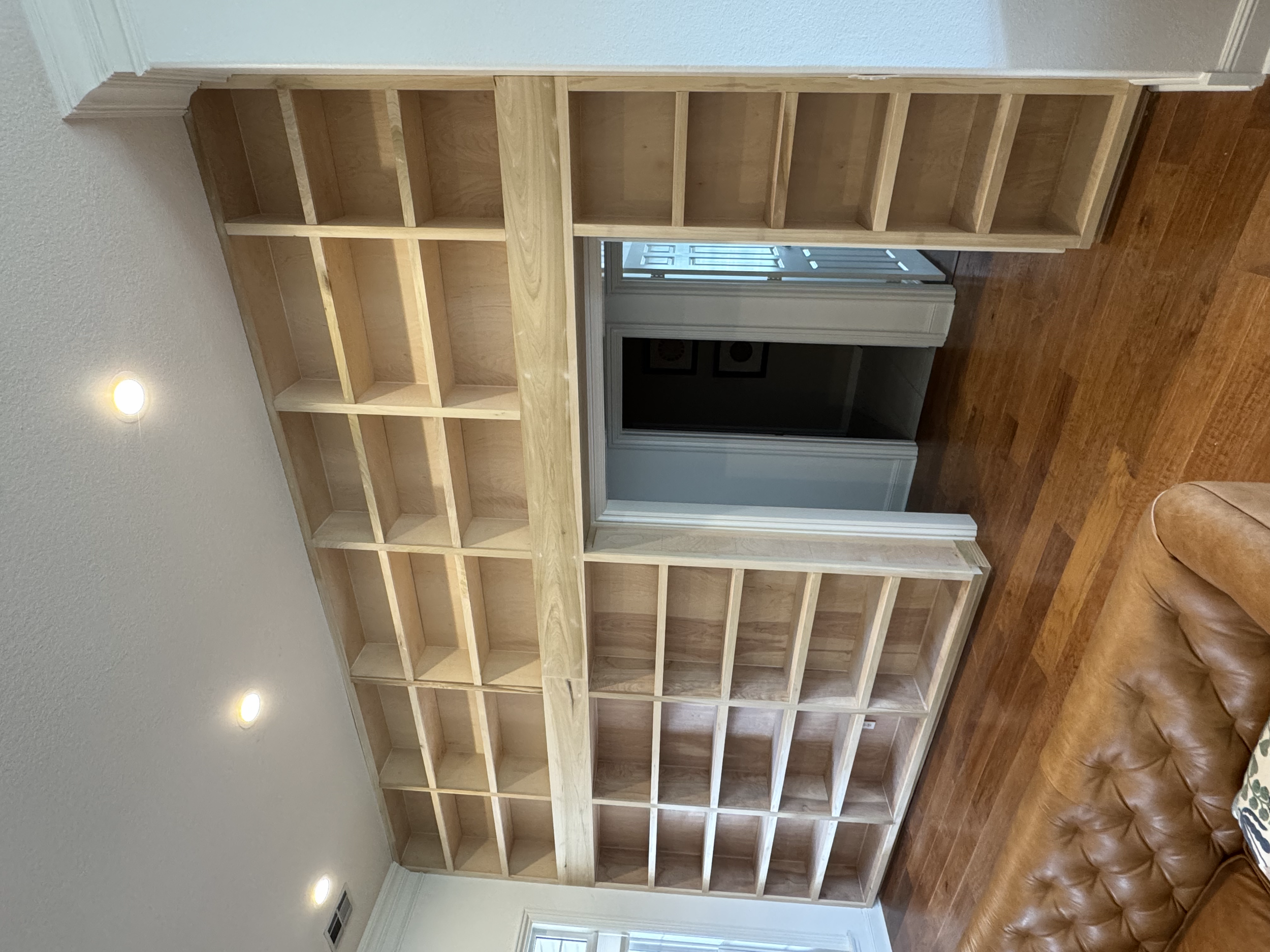 Empty wooden bookshelf inside a room with hardwood flooring and a leather armchair.