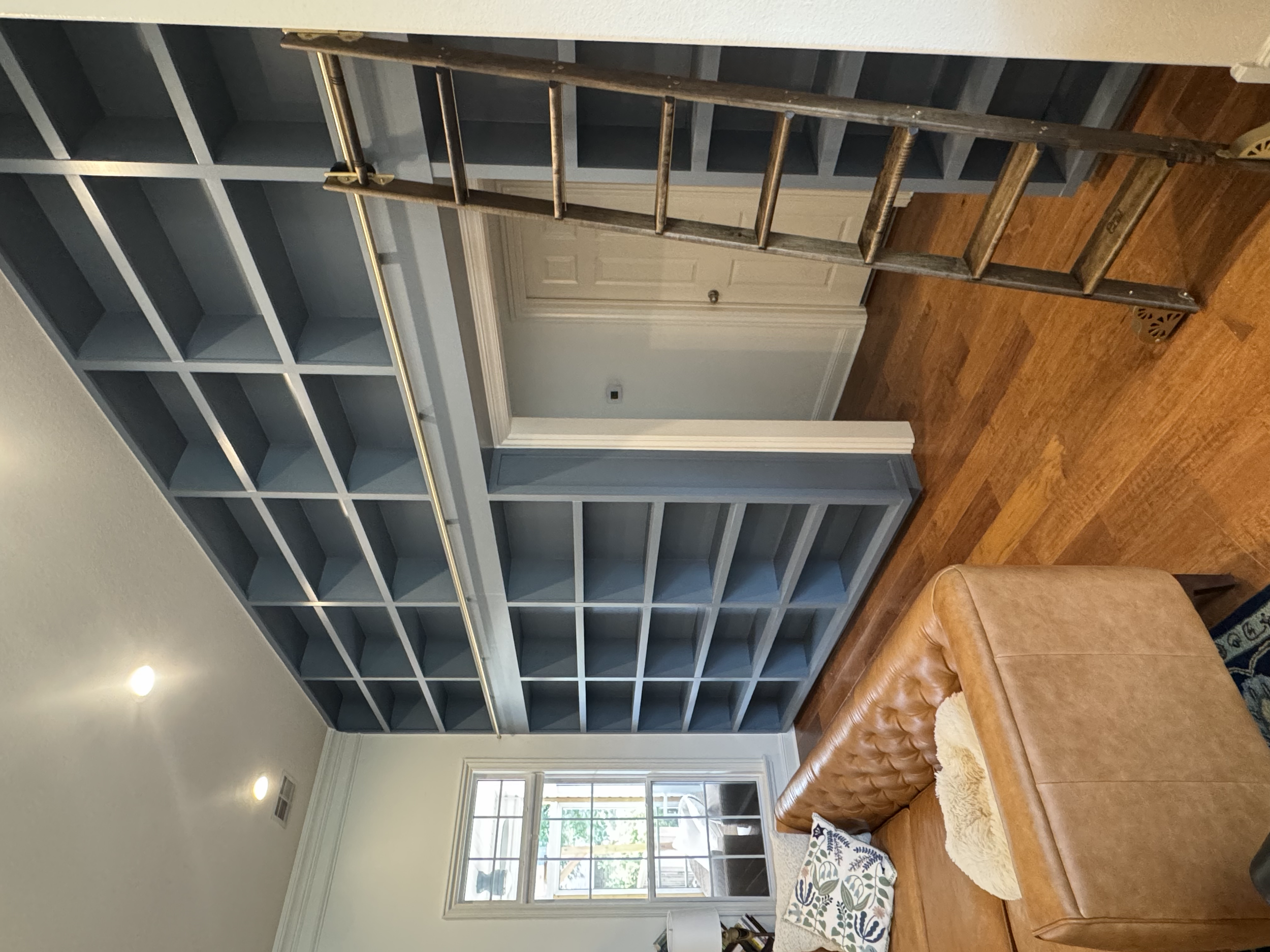 A living room with built-in blue bookshelves, a brown leather sofa, a window with white trim, and hardwood floors.