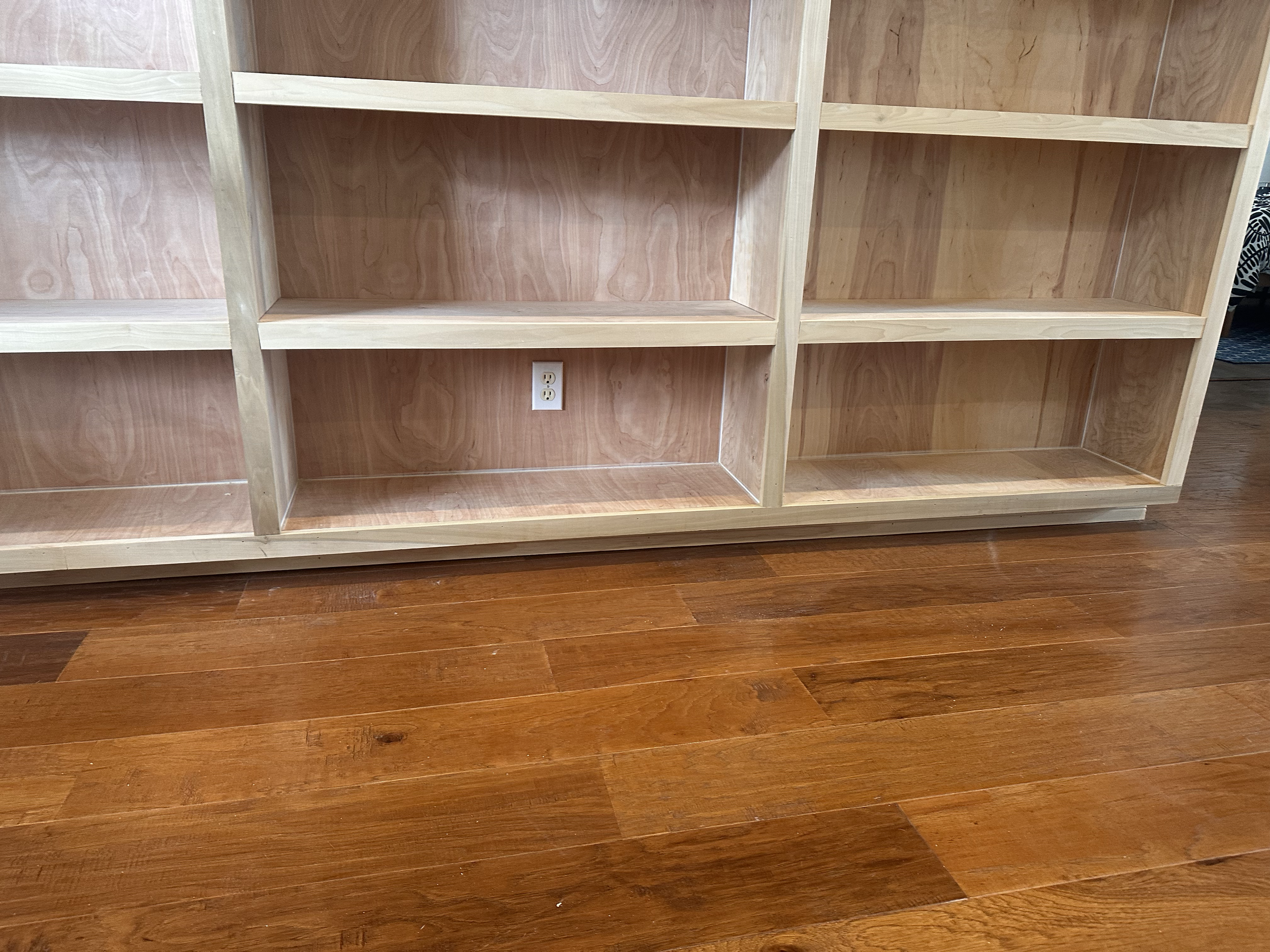 Empty wooden bookshelves with an electrical outlet at the bottom, standing on a polished wooden floor.