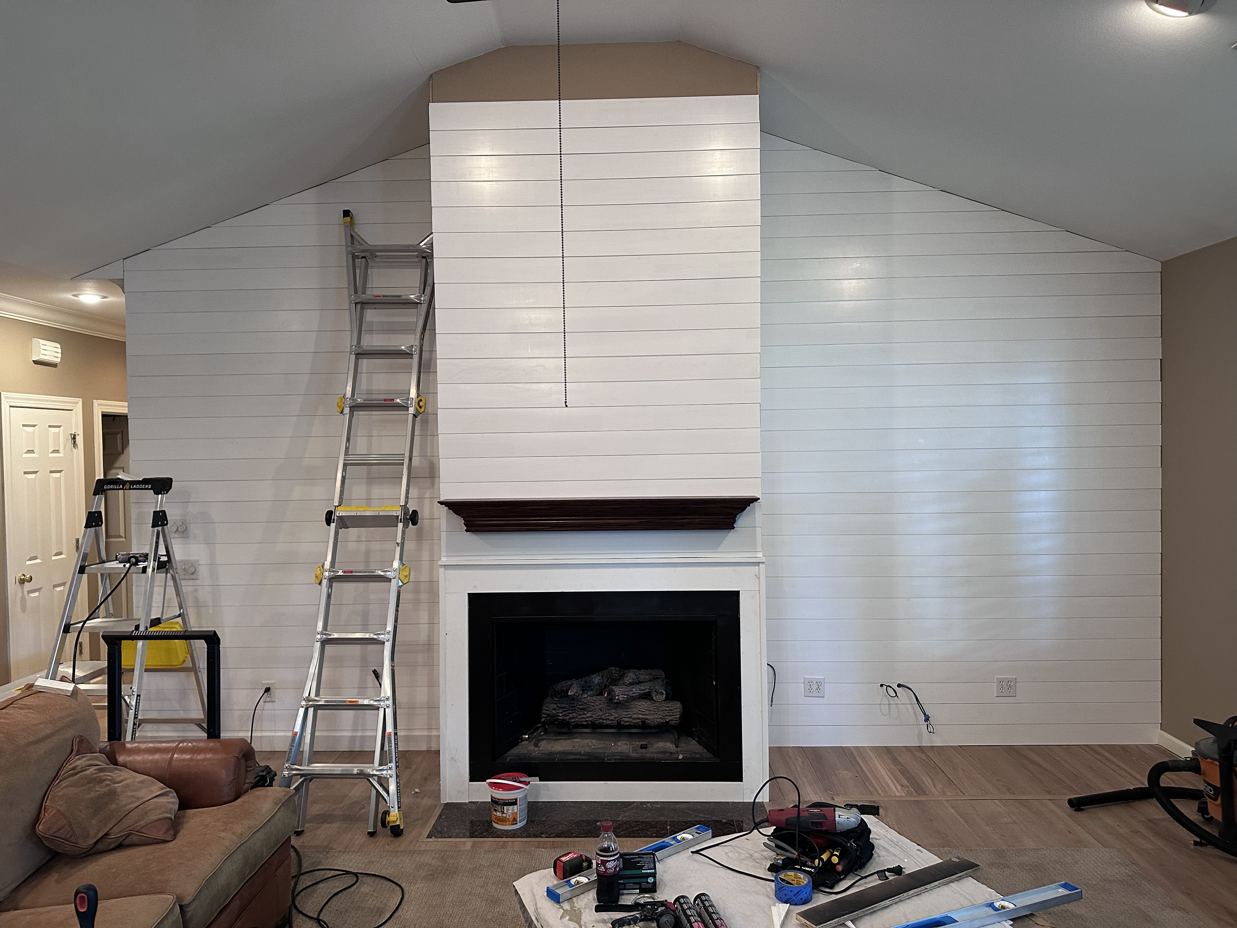 Living room with a fireplace being renovated, with ladders, tools, and construction materials scattered around.