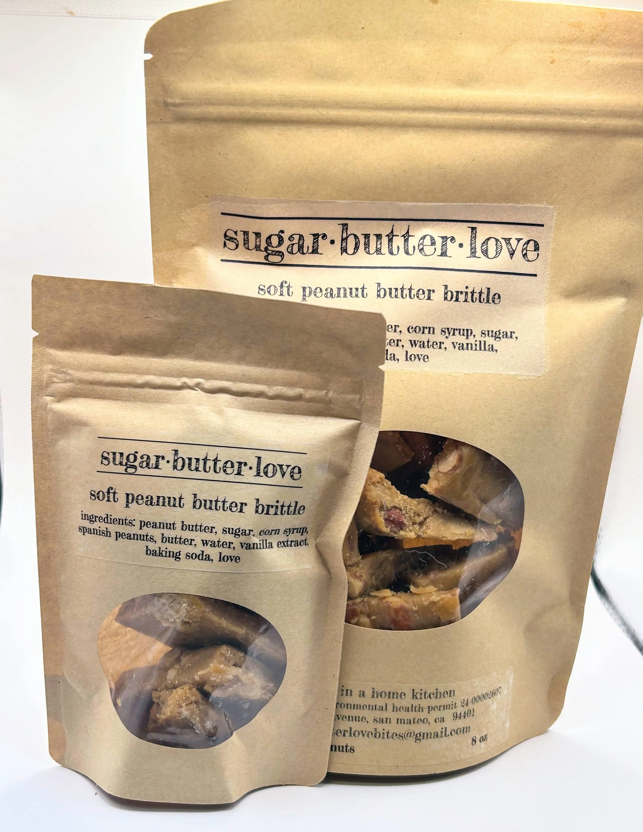 Brown paper bags labeled 'sugar.butter.love' with clear windows showing pieces of soft peanut butter brittle inside.