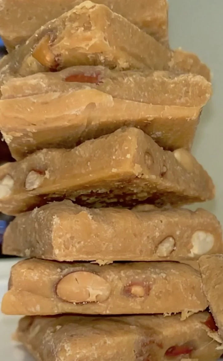 A close-up of stacked pieces of peanut brittle candy with visible nuts and a golden-brown color.