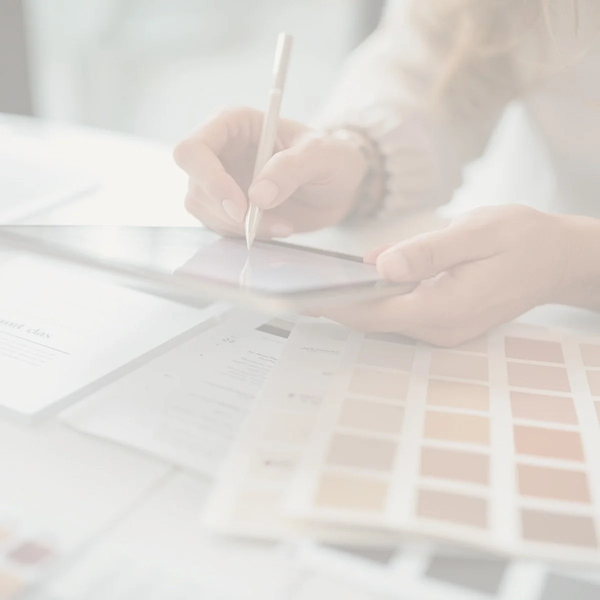 Person using a stylus on a digital tablet with color swatches and design papers on a desk.