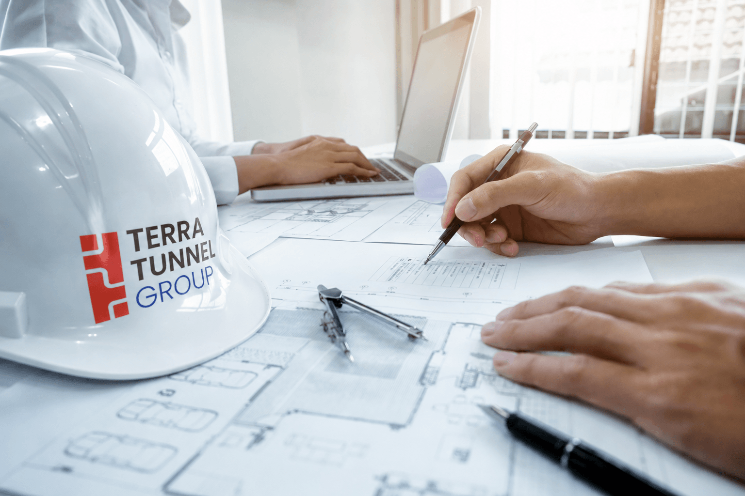 Engineers examining construction blueprints and plans, with a hard hat bearing the Terra Tunnel Group logo.