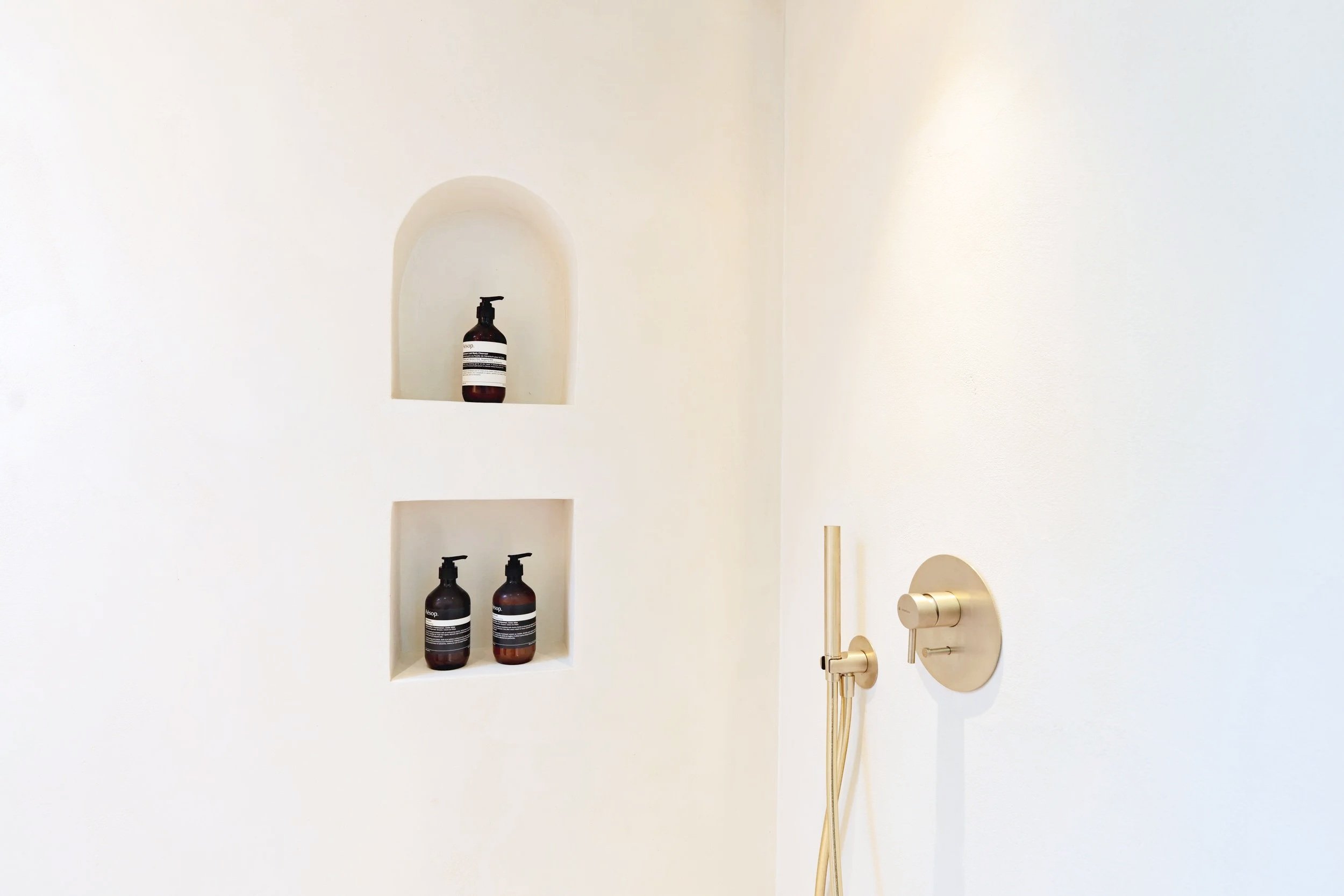 Minimalist bathroom wall with built-in shelves holding three brown bottles and a brass door handle and hinge