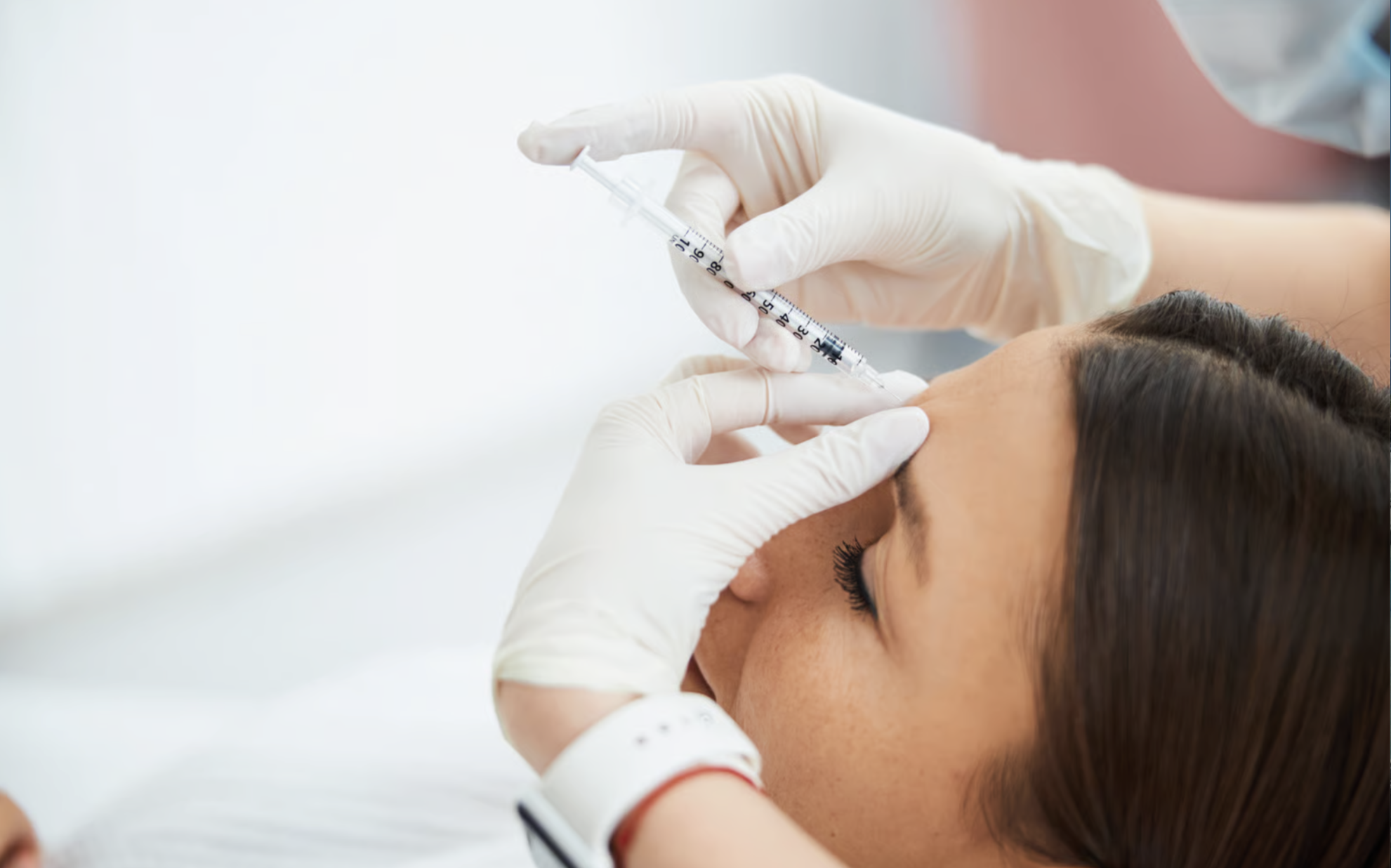 A healthcare professional in gloves administering a vaccination to a woman lying down with her eyes closed.
