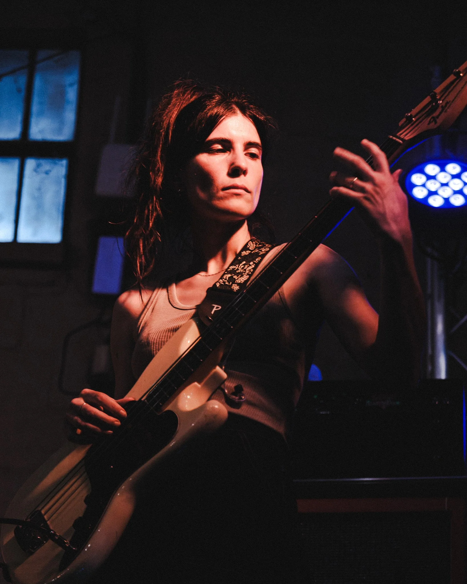 A woman with red hair playing an acoustic guitar on stage, with a dark background and blue stage lights.