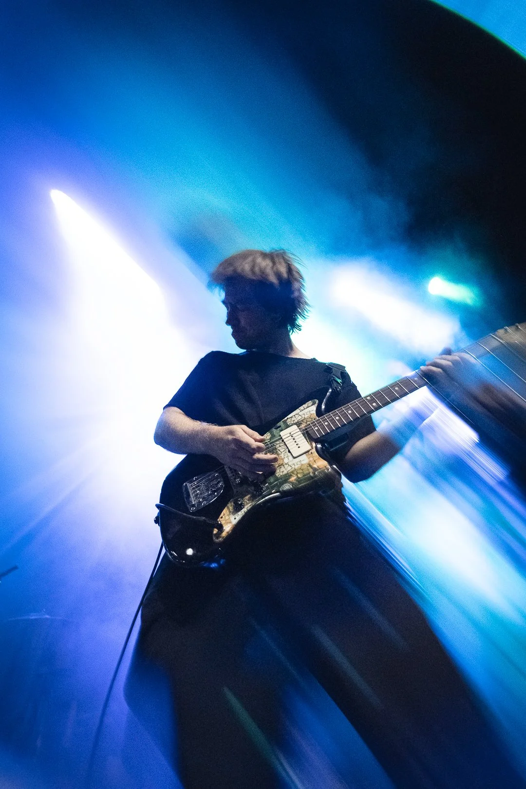 A person playing an electric guitar on stage with colorful lighting and fog, creating a dynamic concert scene.