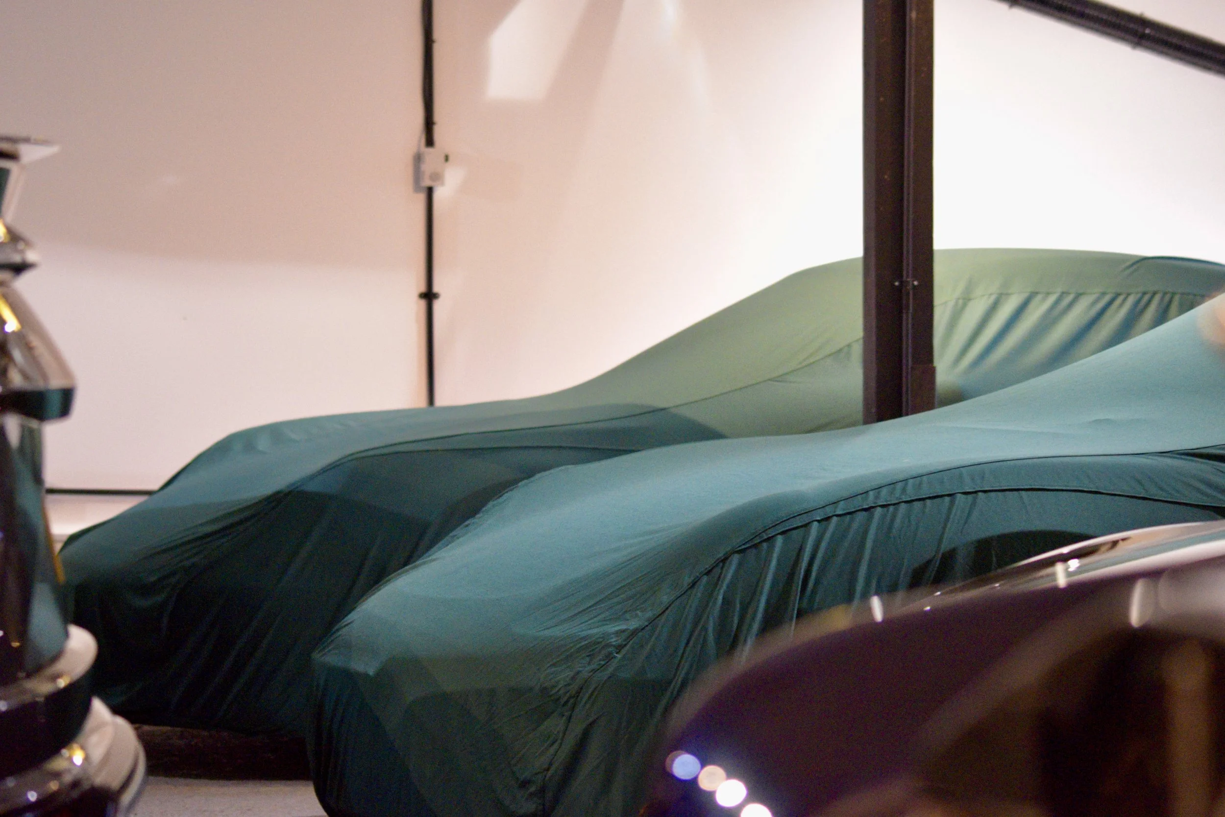 Medical beds with teal sheets in a hospital room, with a white wall and medical equipment nearby.