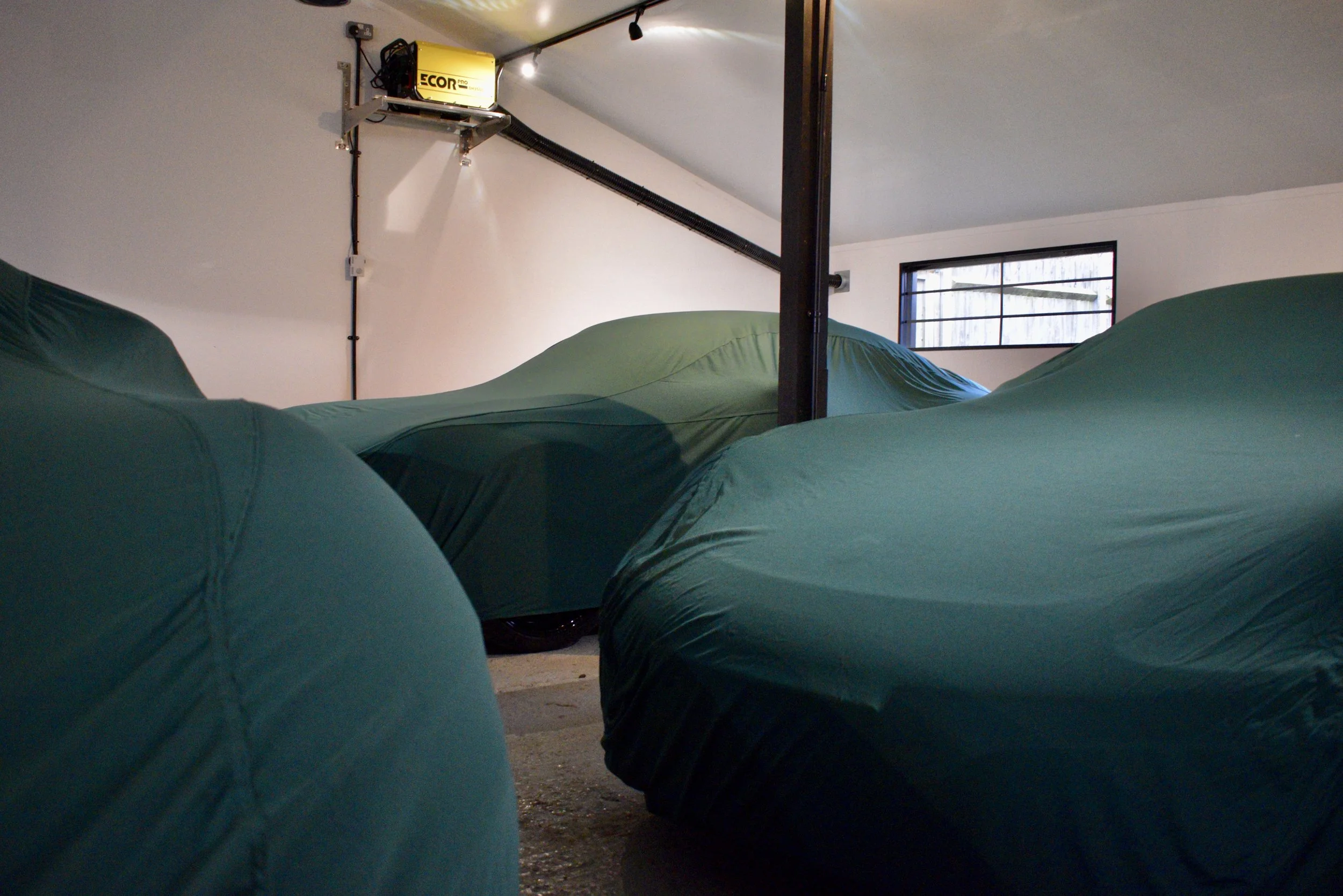 Indoor space with teal bean bag chairs on a concrete floor, a large window with black framing, and a yellow electrical device mounted on the wall near a black cable.