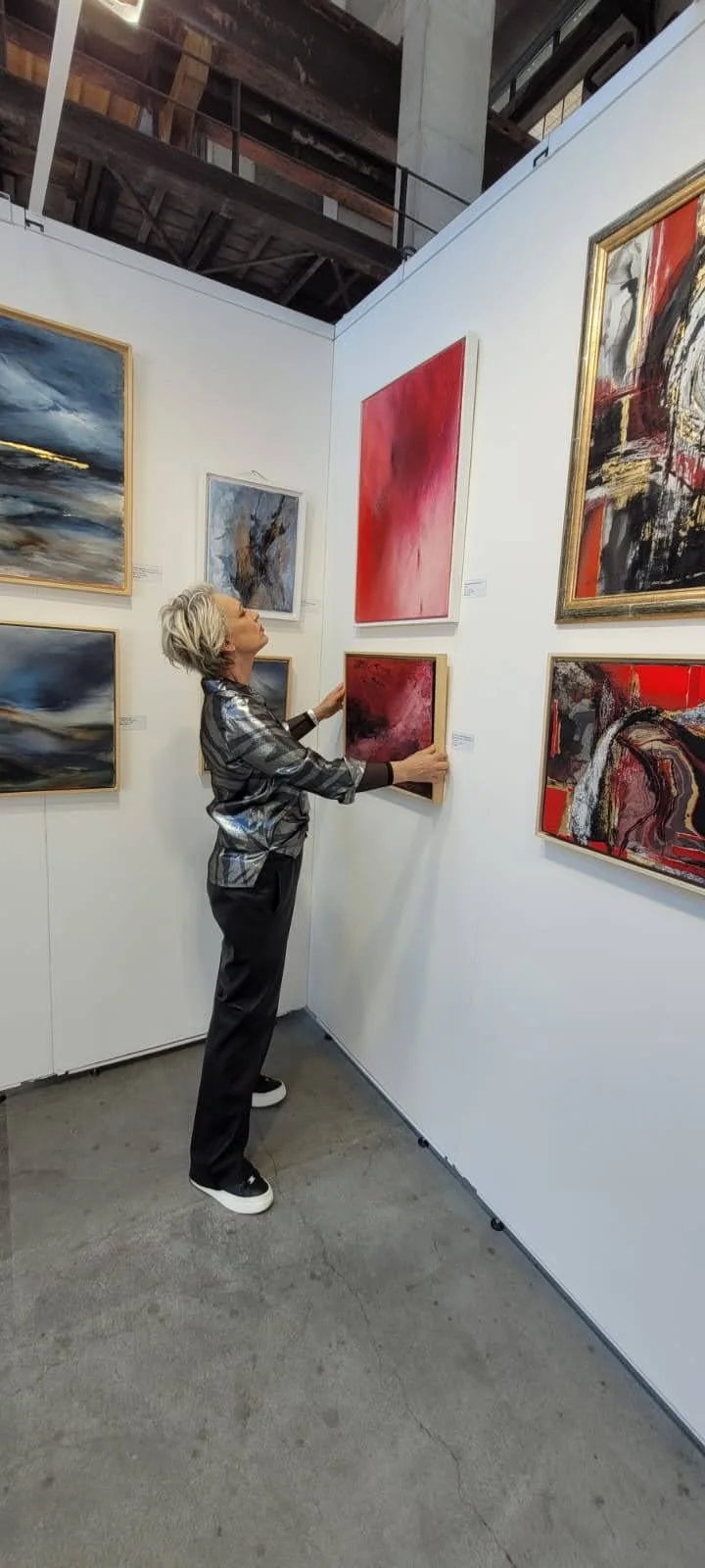 Woman in a gallery viewing abstract paintings with a relaxed posture.