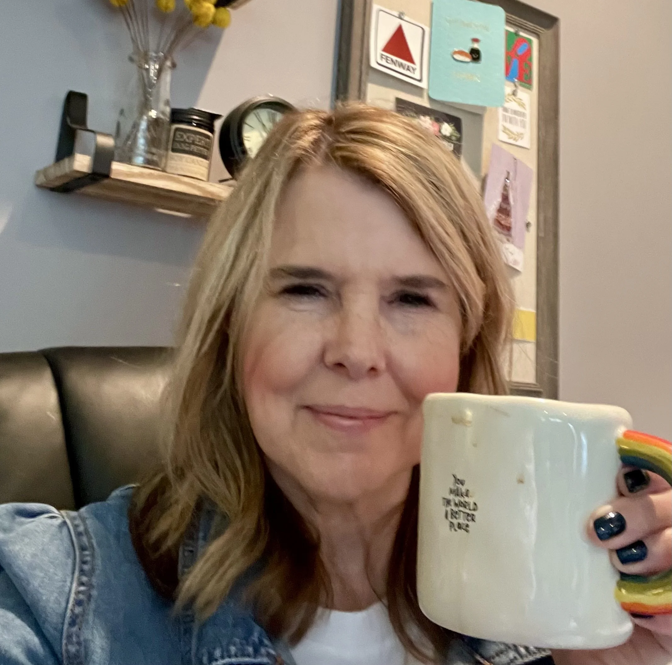 A woman with long, light brown hair smiling while holding a colorful, rainbow-striped cup.