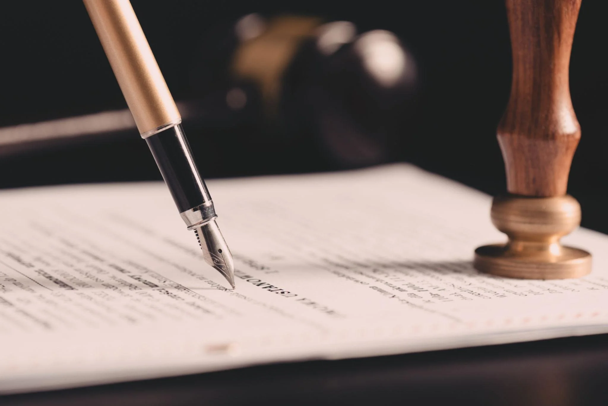 Close-up of a fountain pen writing on a document, with a wooden stamp in the background.
