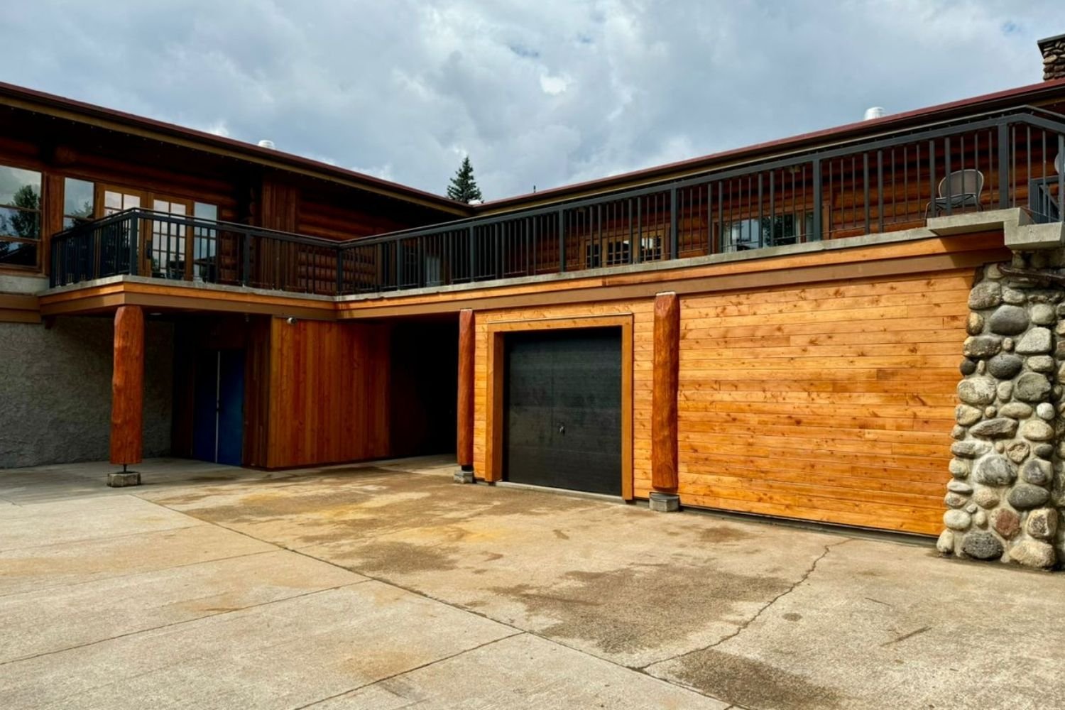 Exterior view of a modern wooden house with a garage, balcony, and stone accents, under cloudy skies. Mtn side general contractor bc albreda lodge renovation