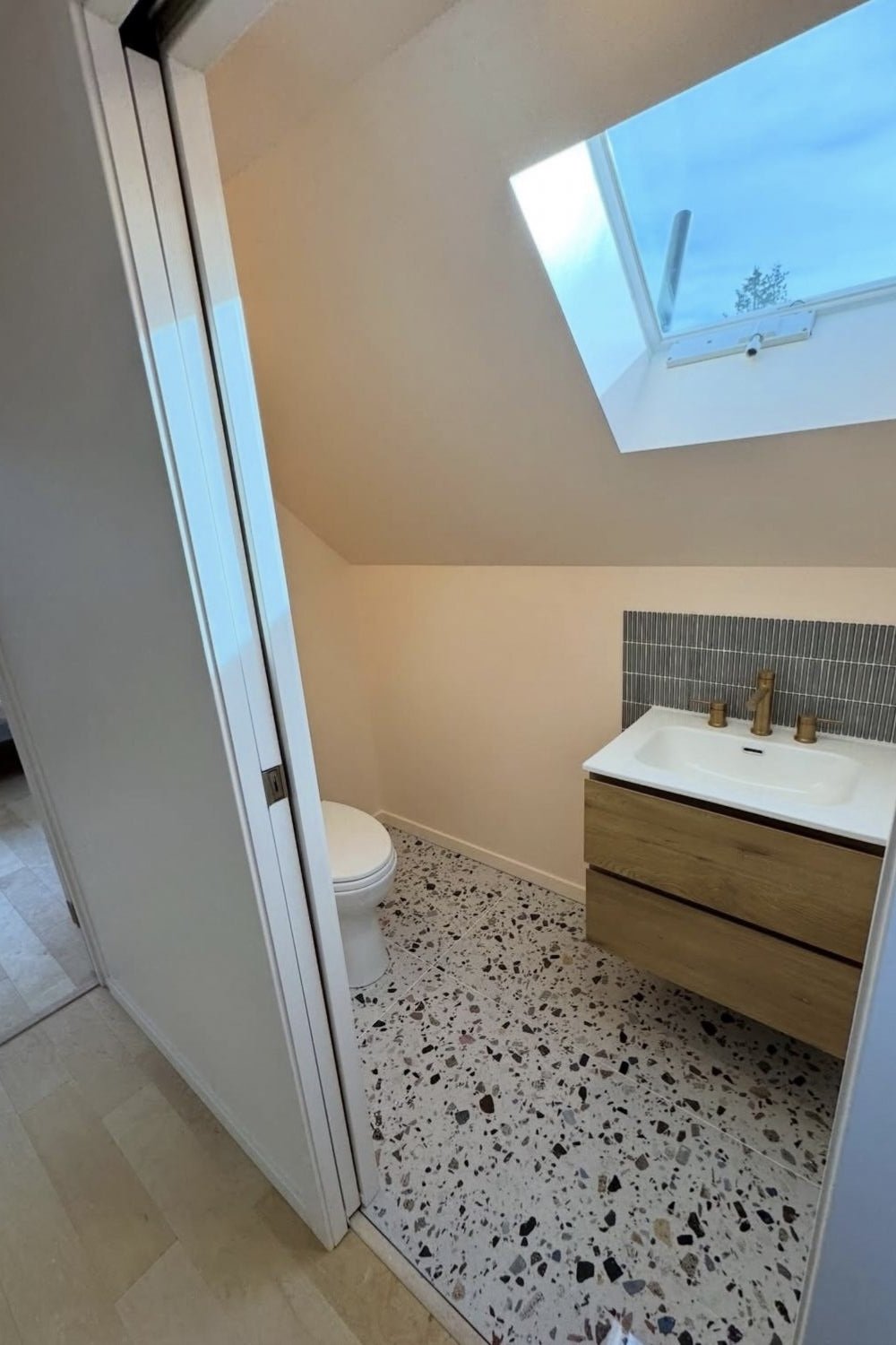 Small bathroom with a skylight, toilet, and wooden vanity with a sink, gray tile backsplash, and terrazzo flooring. Mtn Side general contractor bathroom residential work
