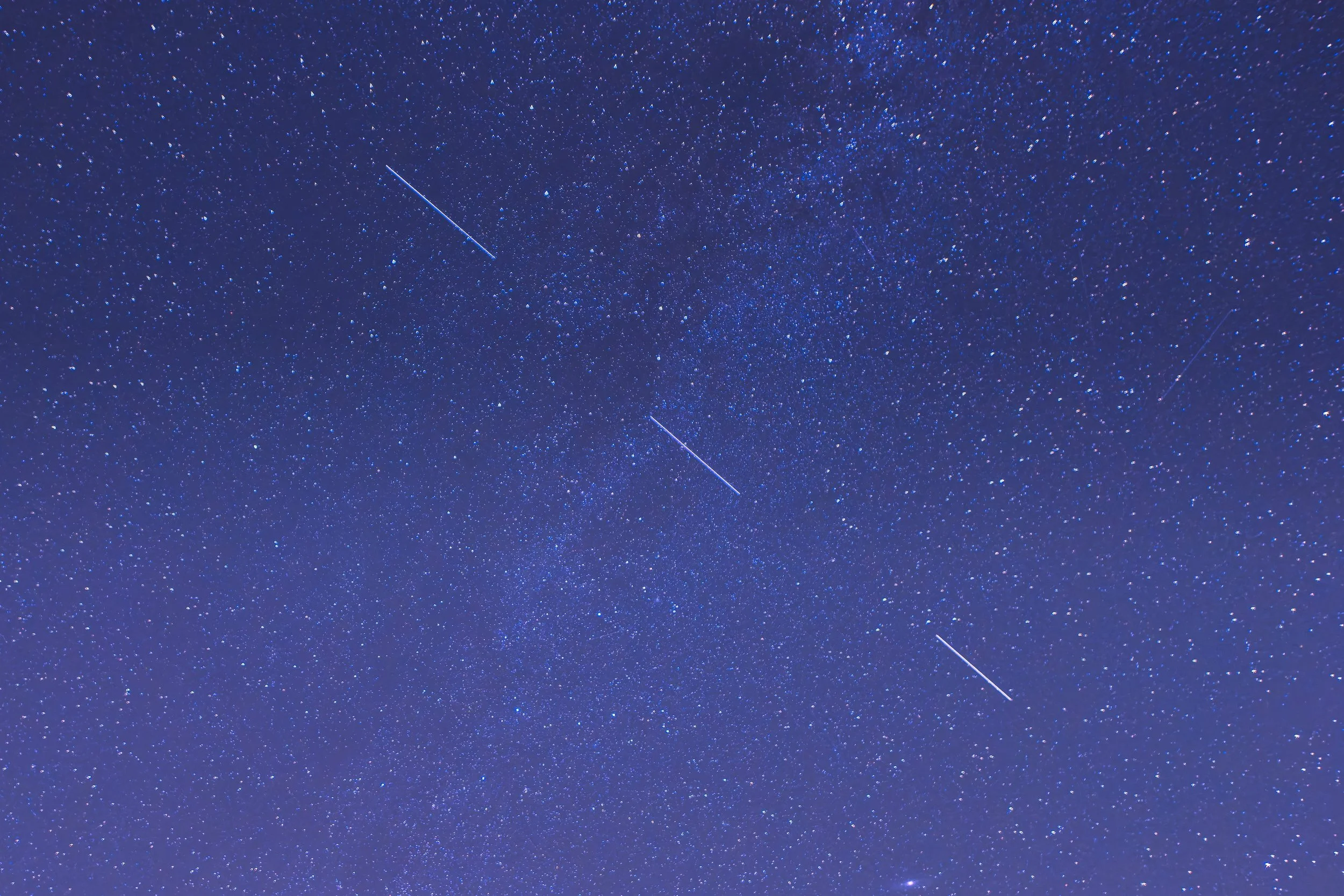 Een nachtelijke hemel vol sterren met een meteoor die door de lucht schiet.