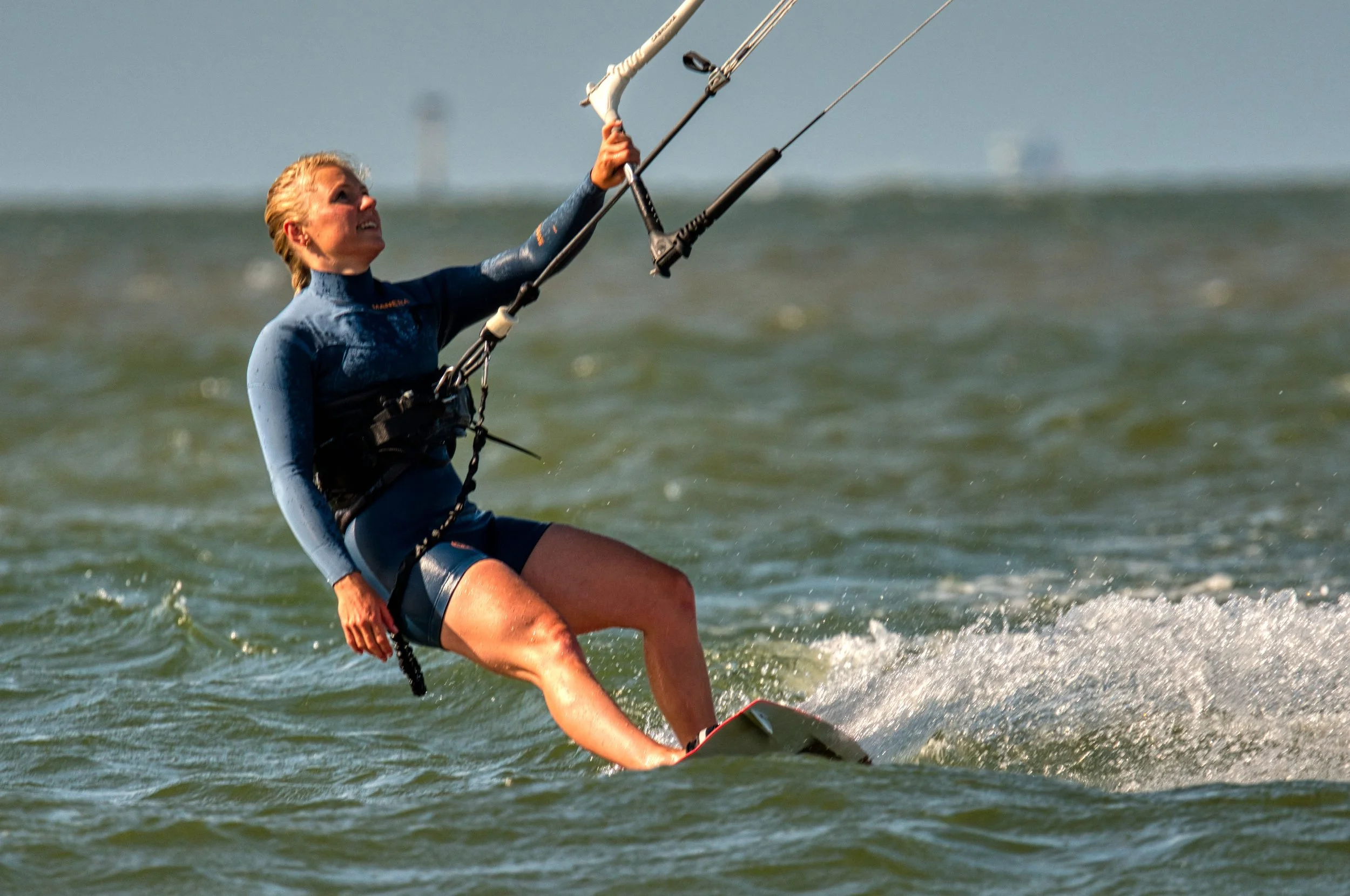 Vrouw kitesurfen op zee met blauwe wetsuit en parasail in de lucht.