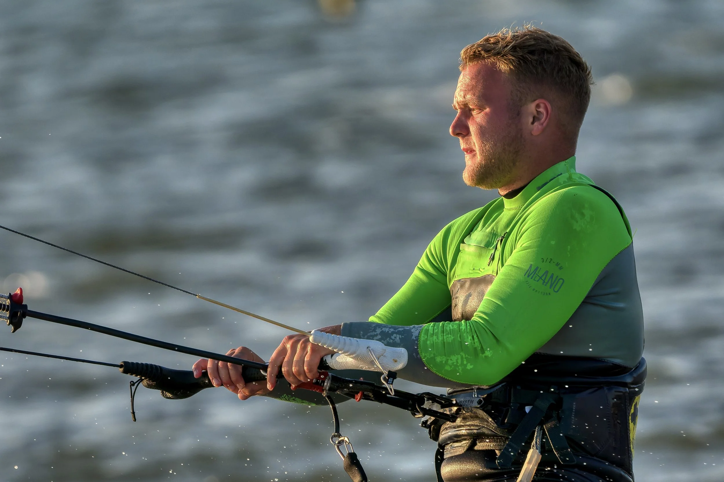 Man viste een groene wetsuit en vist met een hengel op het water.
