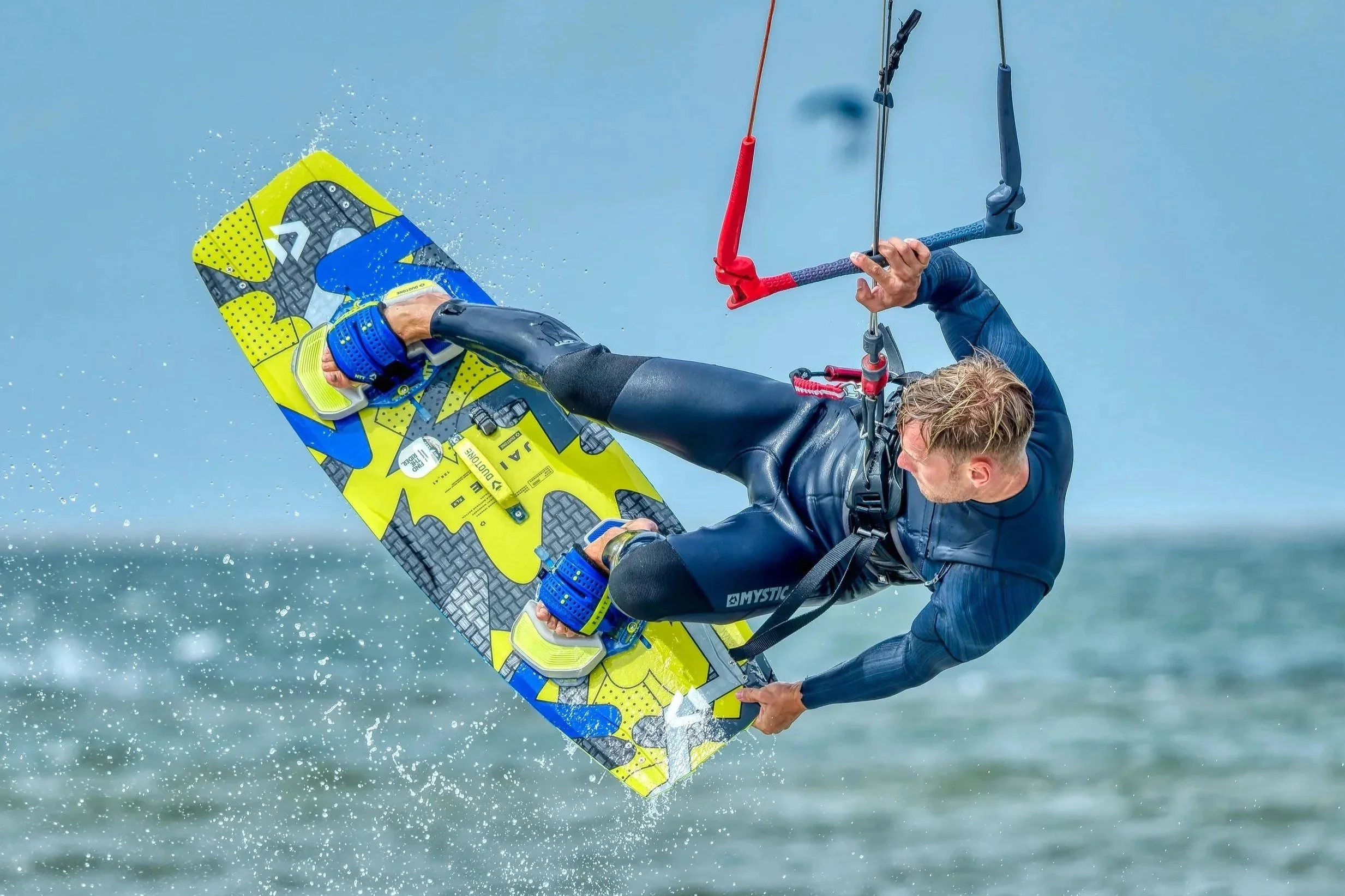 Een surfer die een sprong maakt boven het water met een gele en blauwe surfplank.