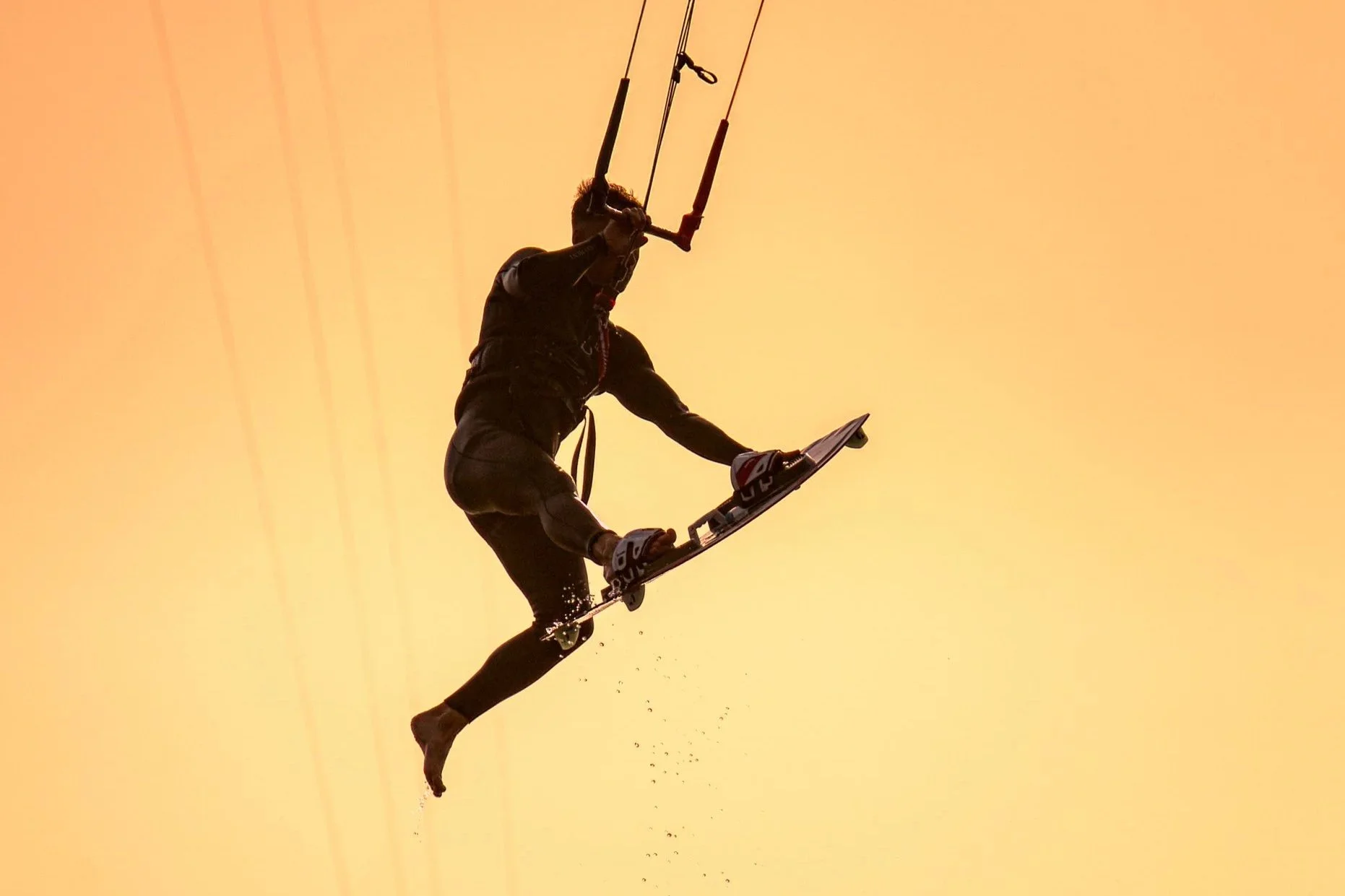 Een persoon die wakeboardt tijdens zonsondergang, lichaamsgewicht naar beneden gebogen, met het water onder zich en de lucht in een geel-oranje tint.