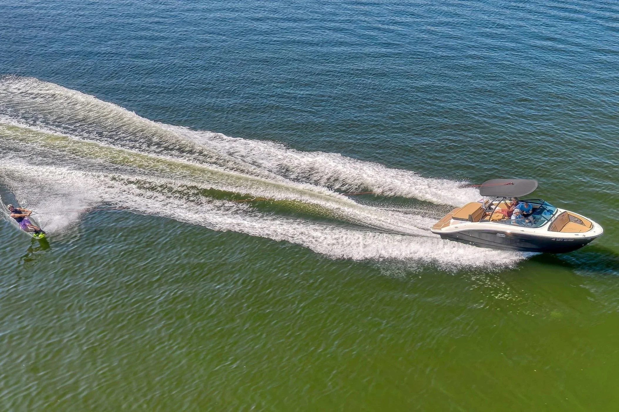 Een speedboot met meerdere mensen die op het water hangen, inclusief een persoon die aan een waterski trekt.