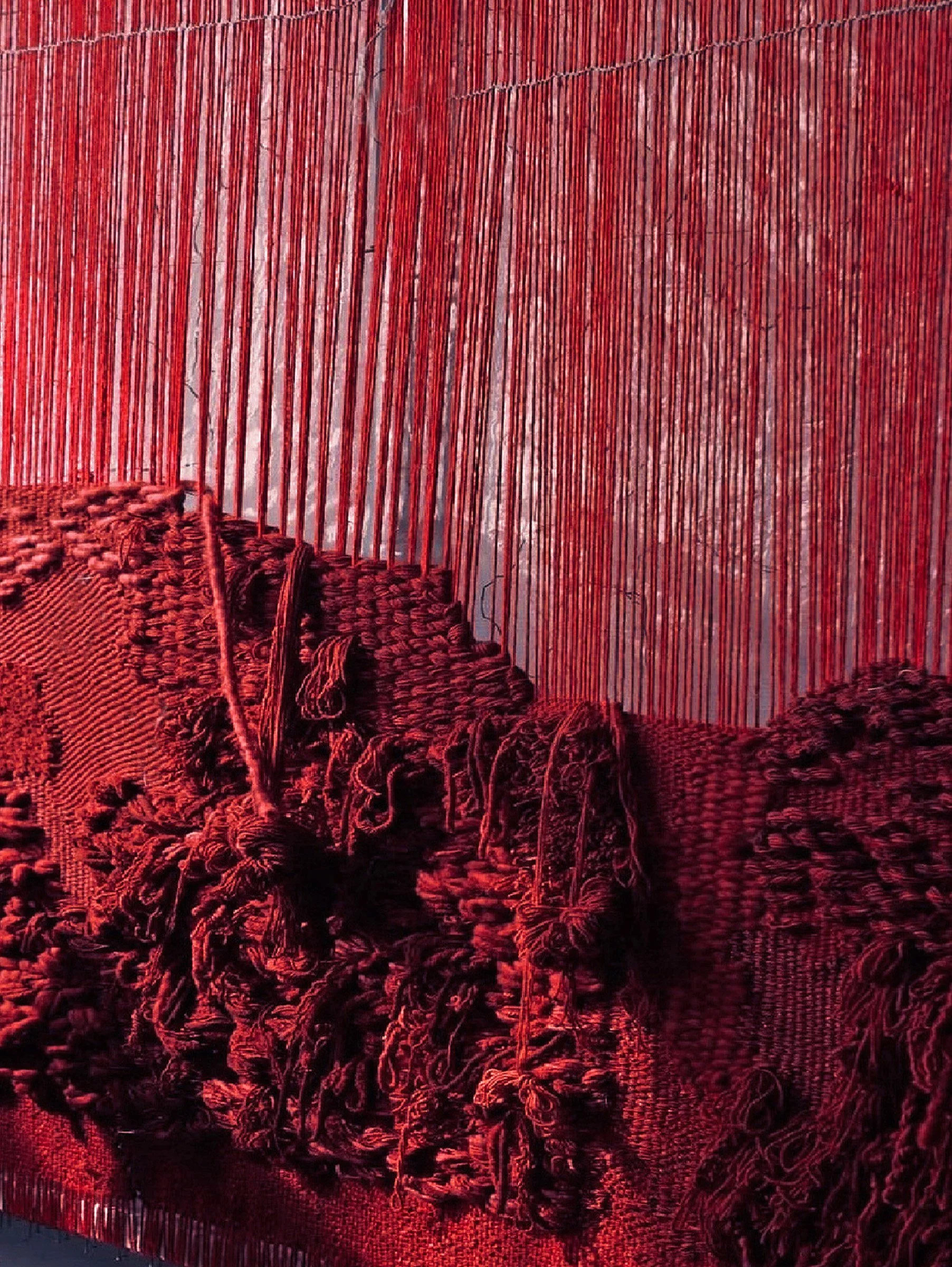 Red wool weaving process with suspended yarn structures and densely layered woven fibre in progress