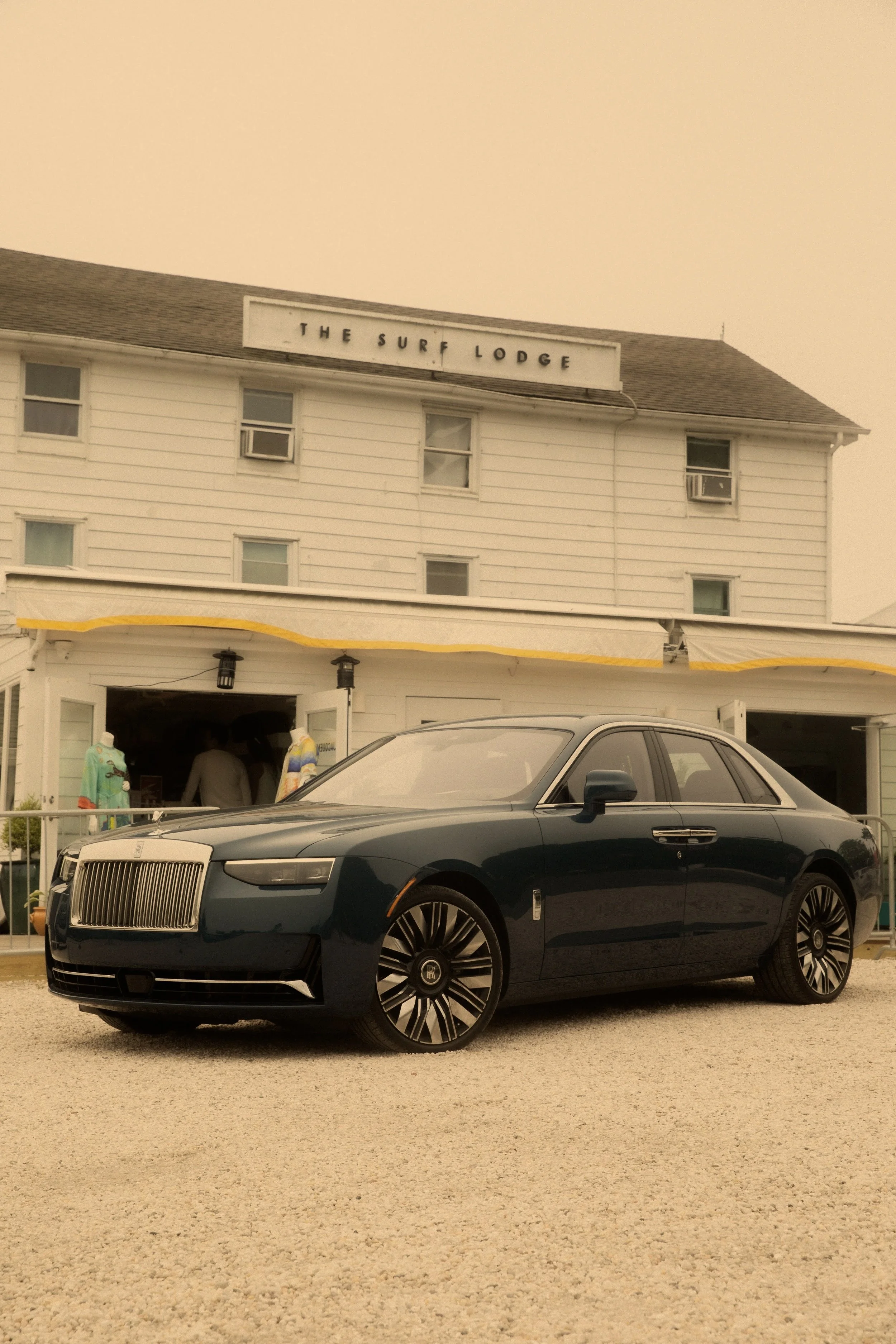 Luxury black car parked in front of a white building with a sign that reads 'The Surf Lodge'.