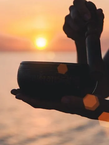 A person holding a cup, with a sunset over water in the background.