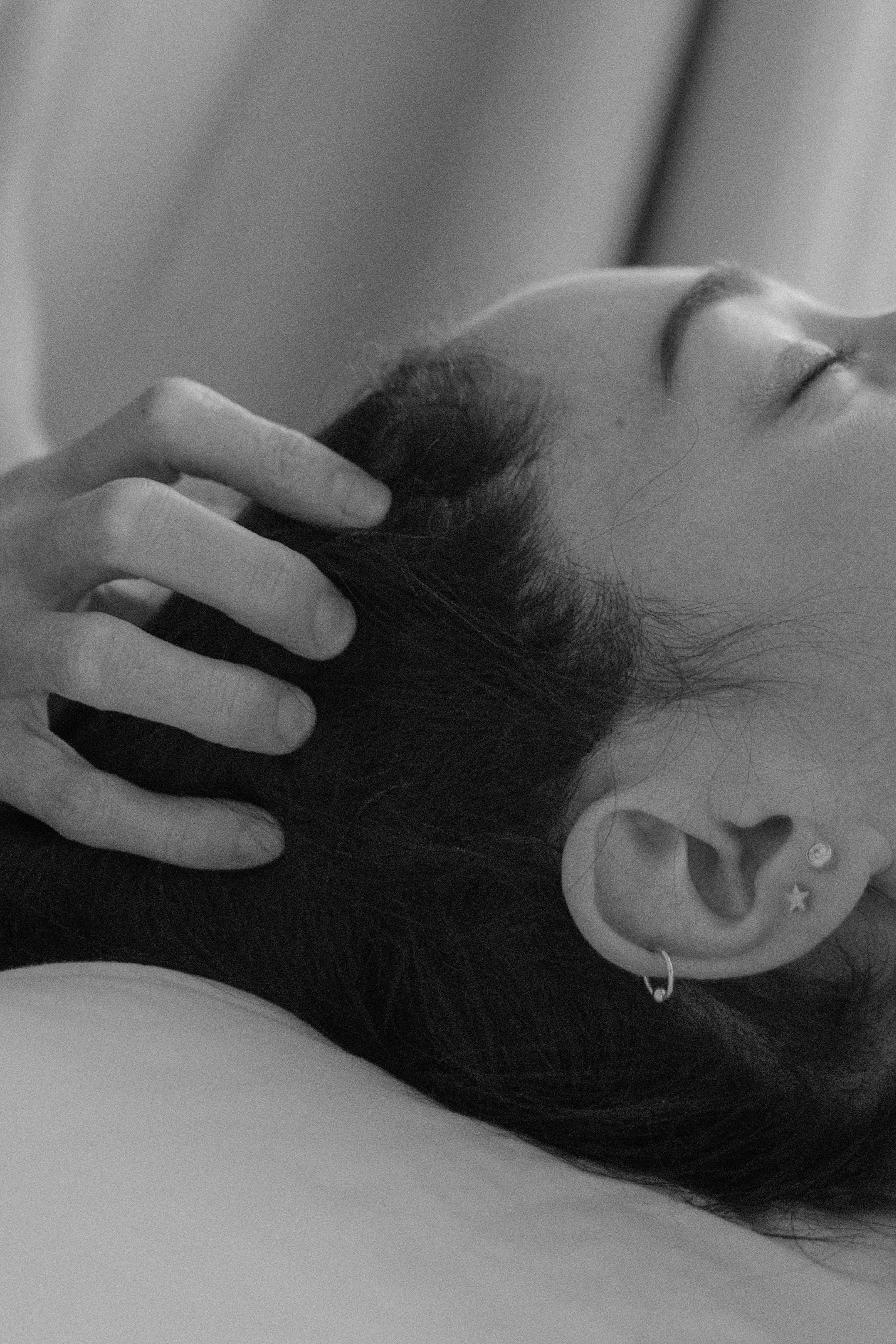 Close-up of a woman with earrings in her ear, with her eyes closed, resting her hand on her head.