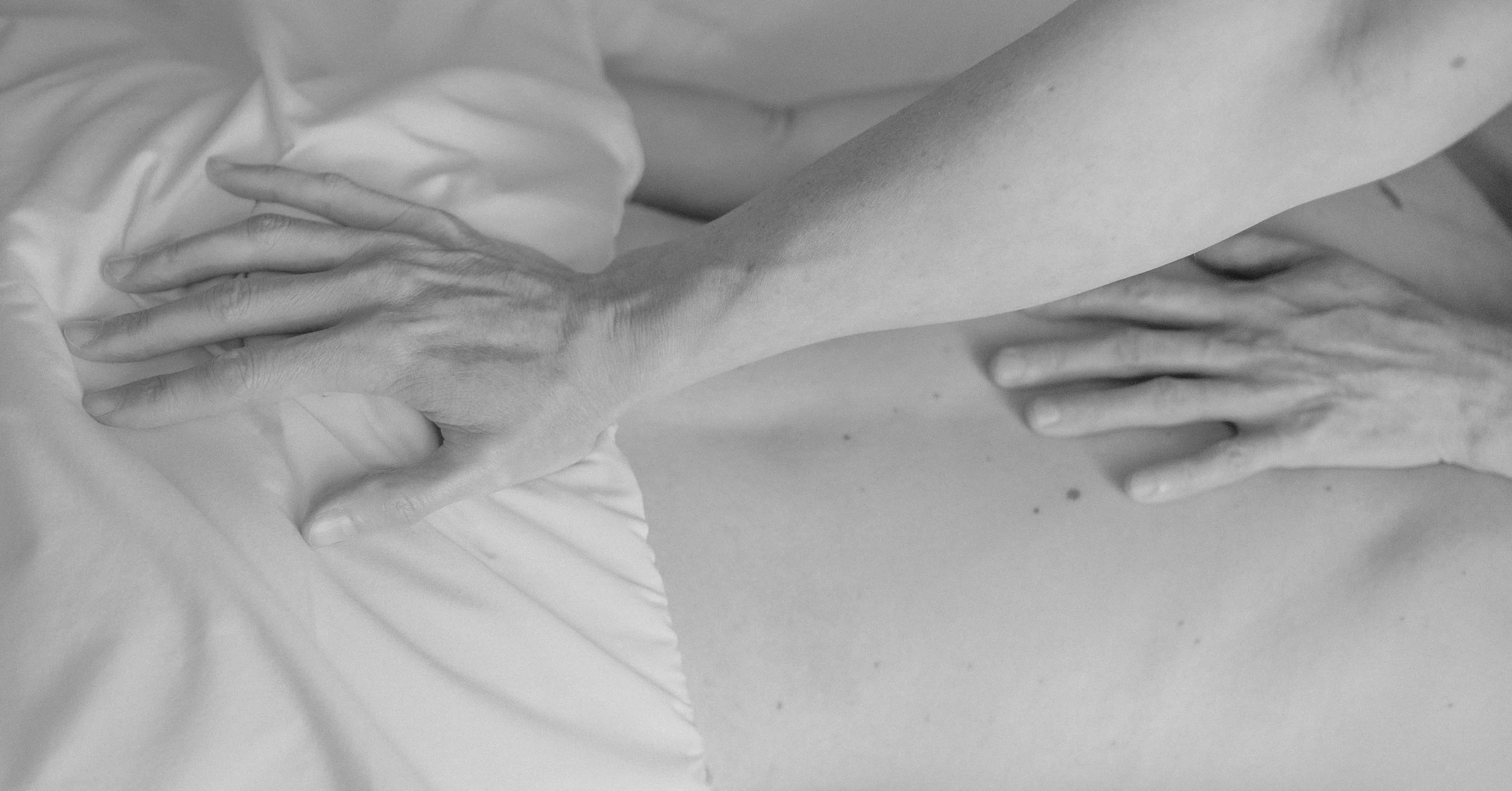 Close-up view of two hands pressing on a soft surface, possibly a bed or a cushion, with a person wearing a white shirt visible in the background.